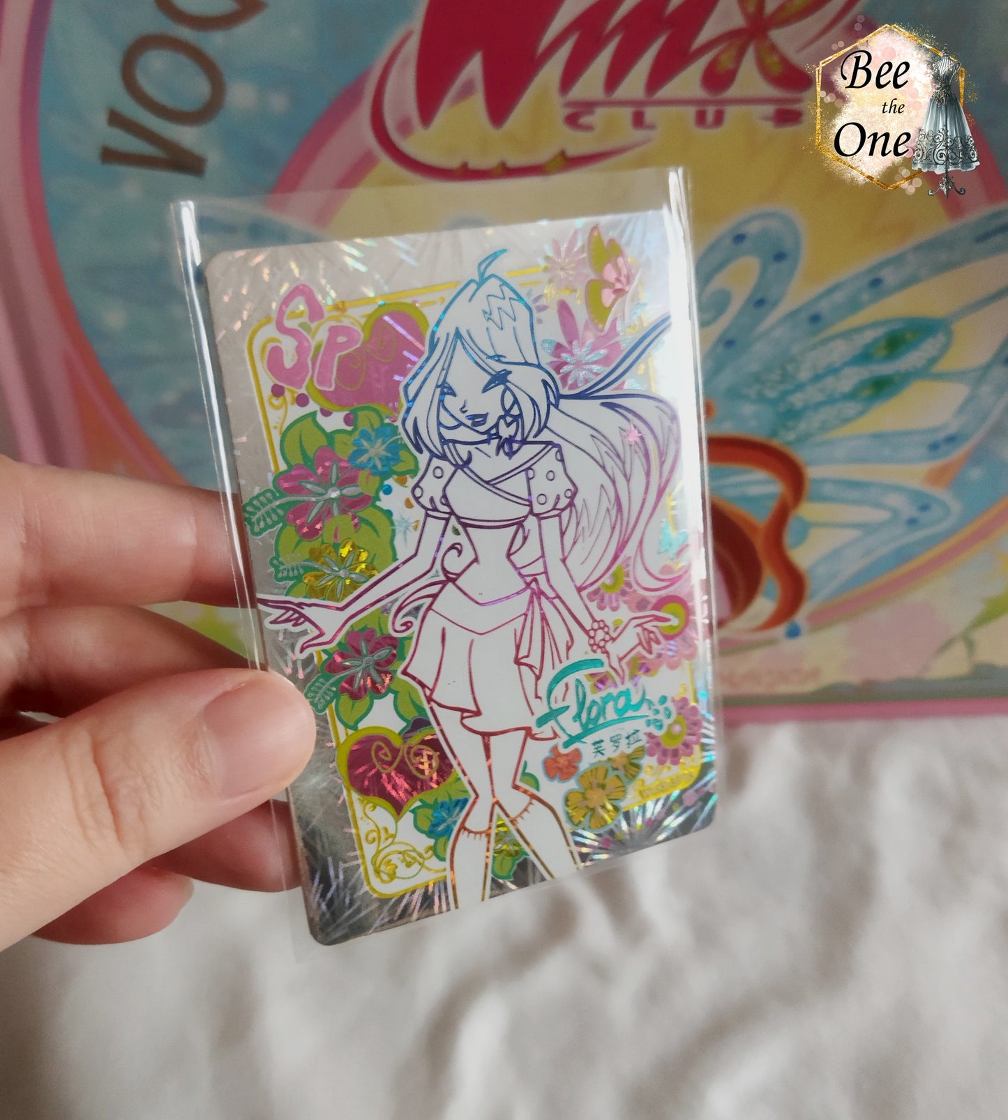 Carte de collection Winx Club brillante type hologramme représentant la fée Flora, édition spéciale SP avec illustrations de fleurs exotiques et cœurs colorés. Gros plan