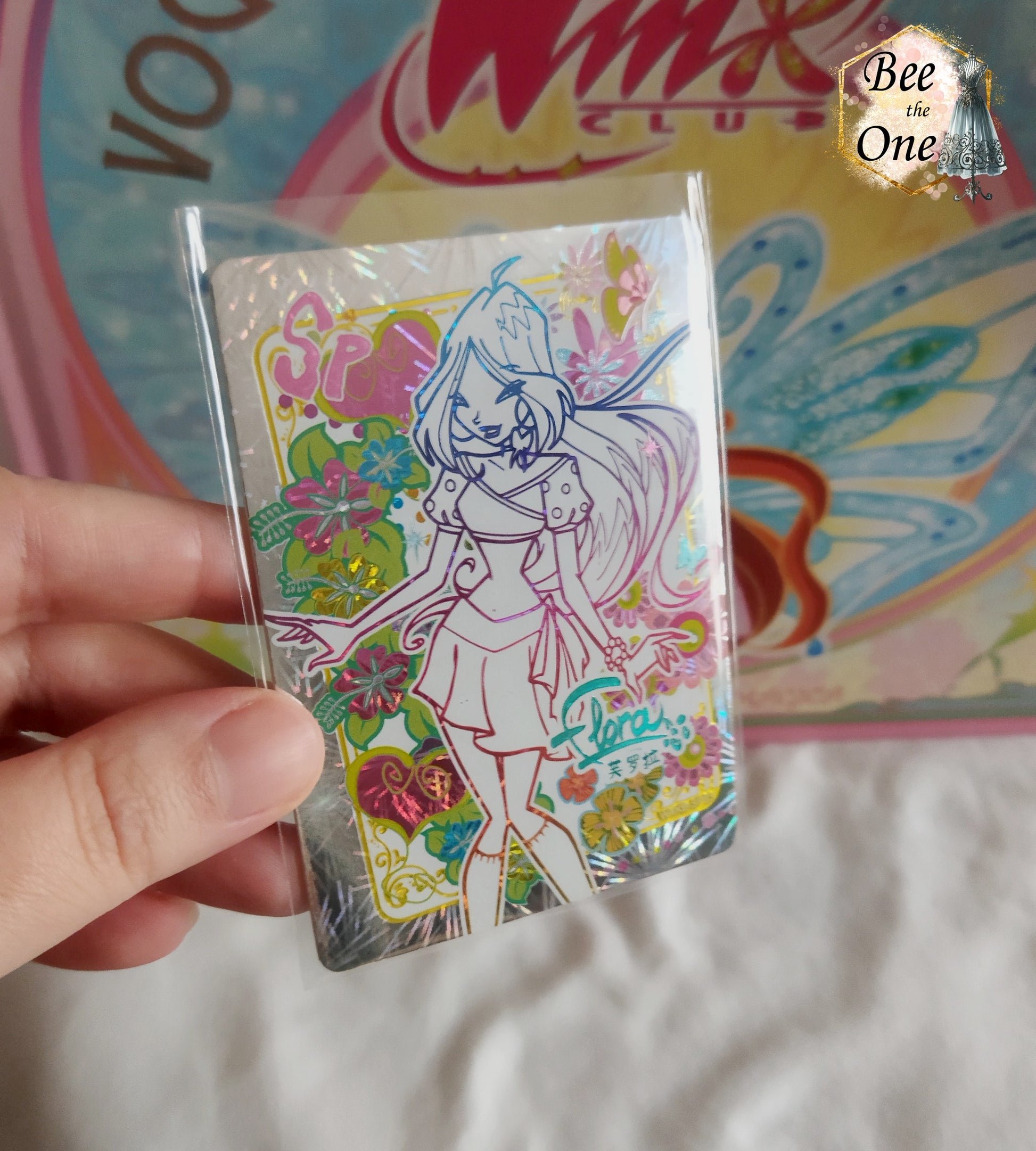 Carte de collection Winx Club brillante type hologramme représentant la fée Flora, édition spéciale SP avec illustrations de fleurs exotiques et cœurs colorés. Gros plan