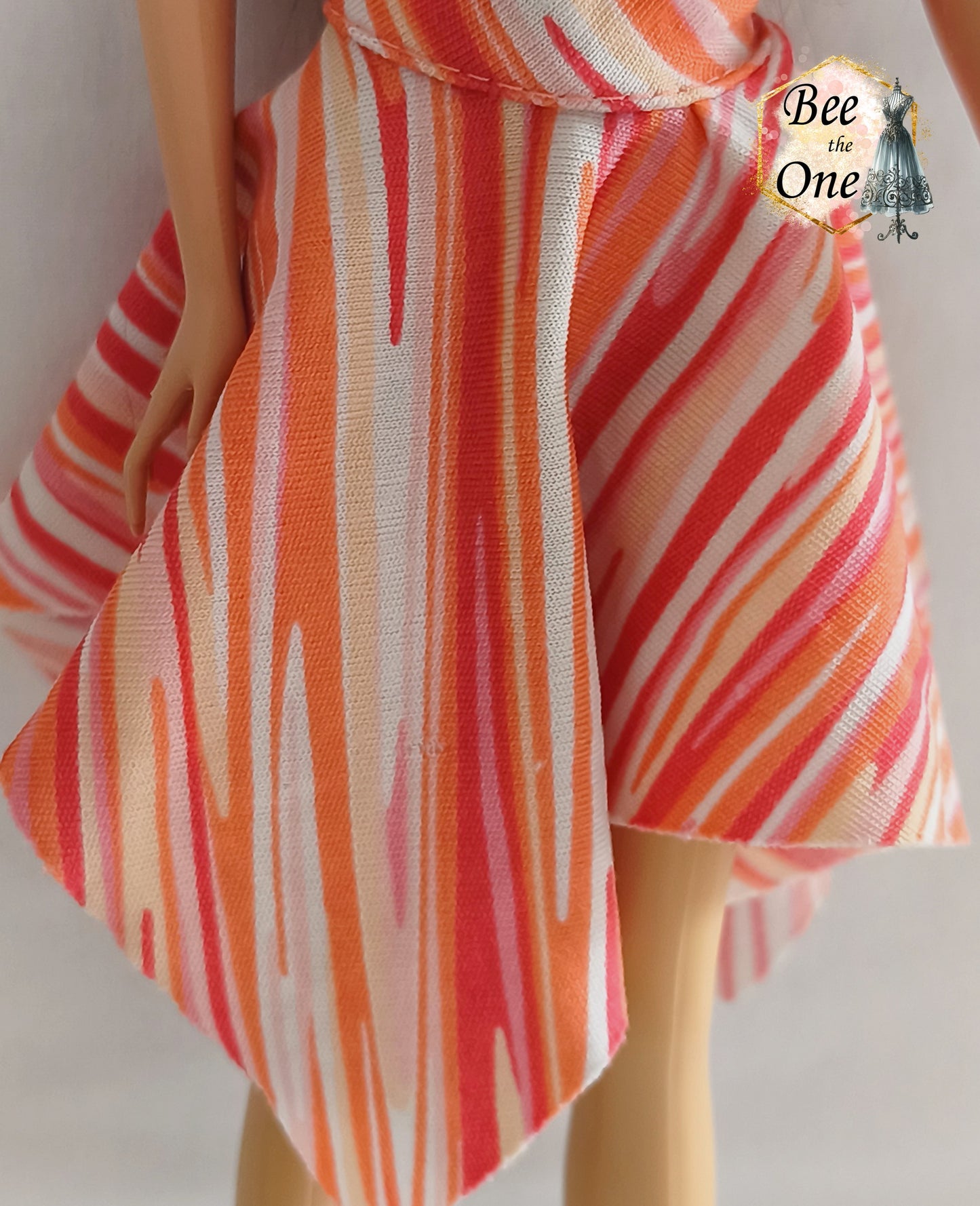 Robe asymétrique pour poupée mannequin Barbie Fashion Fever 2005, dos-nu à motifs géométriques corail, rose et orange avec attache argentée, présenté sur mannequin et fond blanc. Gros plan jupe