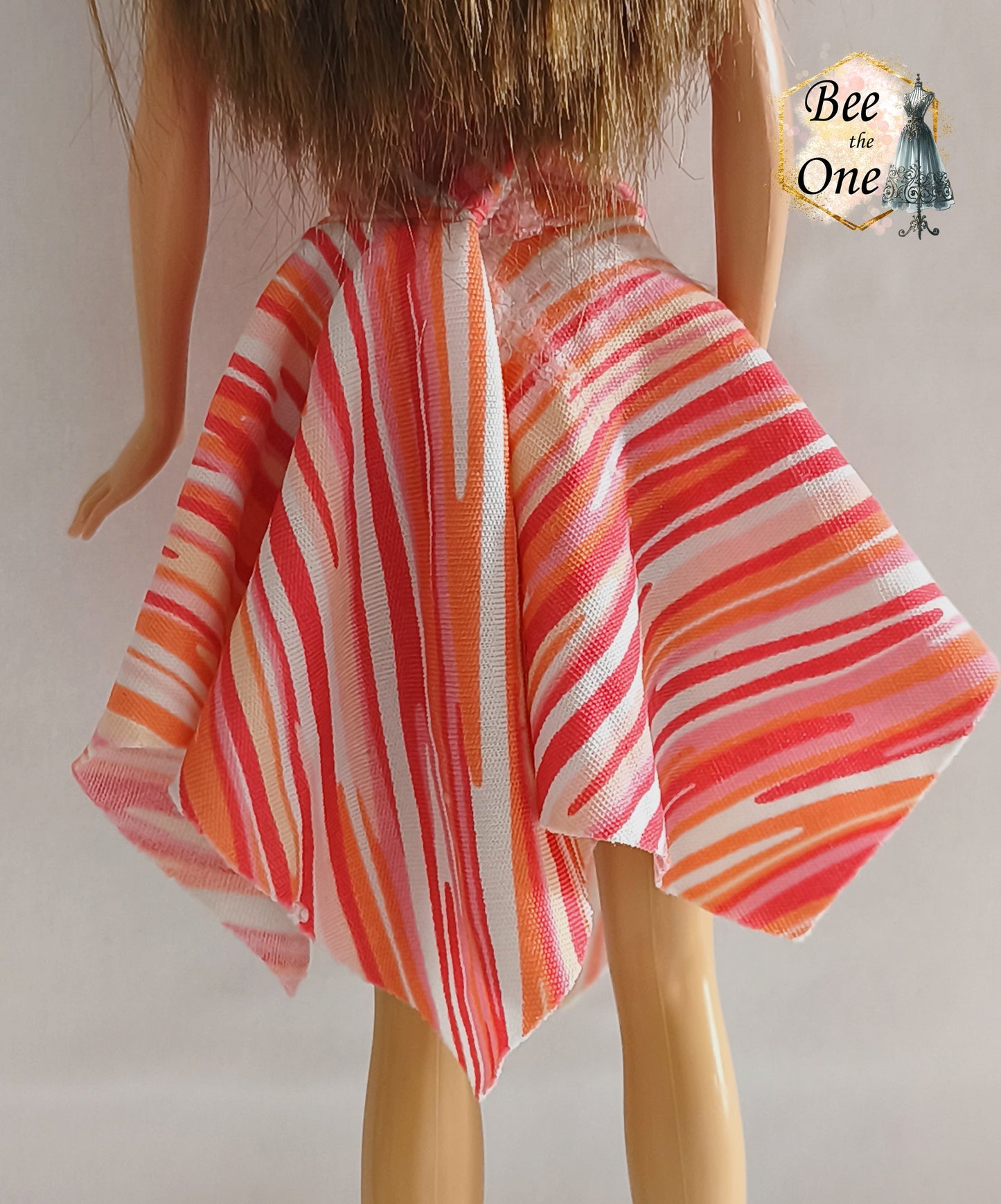 Robe asymétrique pour poupée mannequin Barbie Fashion Fever 2005, dos-nu à motifs géométriques corail, rose et orange avec attache argentée, présenté sur mannequin et fond blanc. Gros plan dos de la jupe