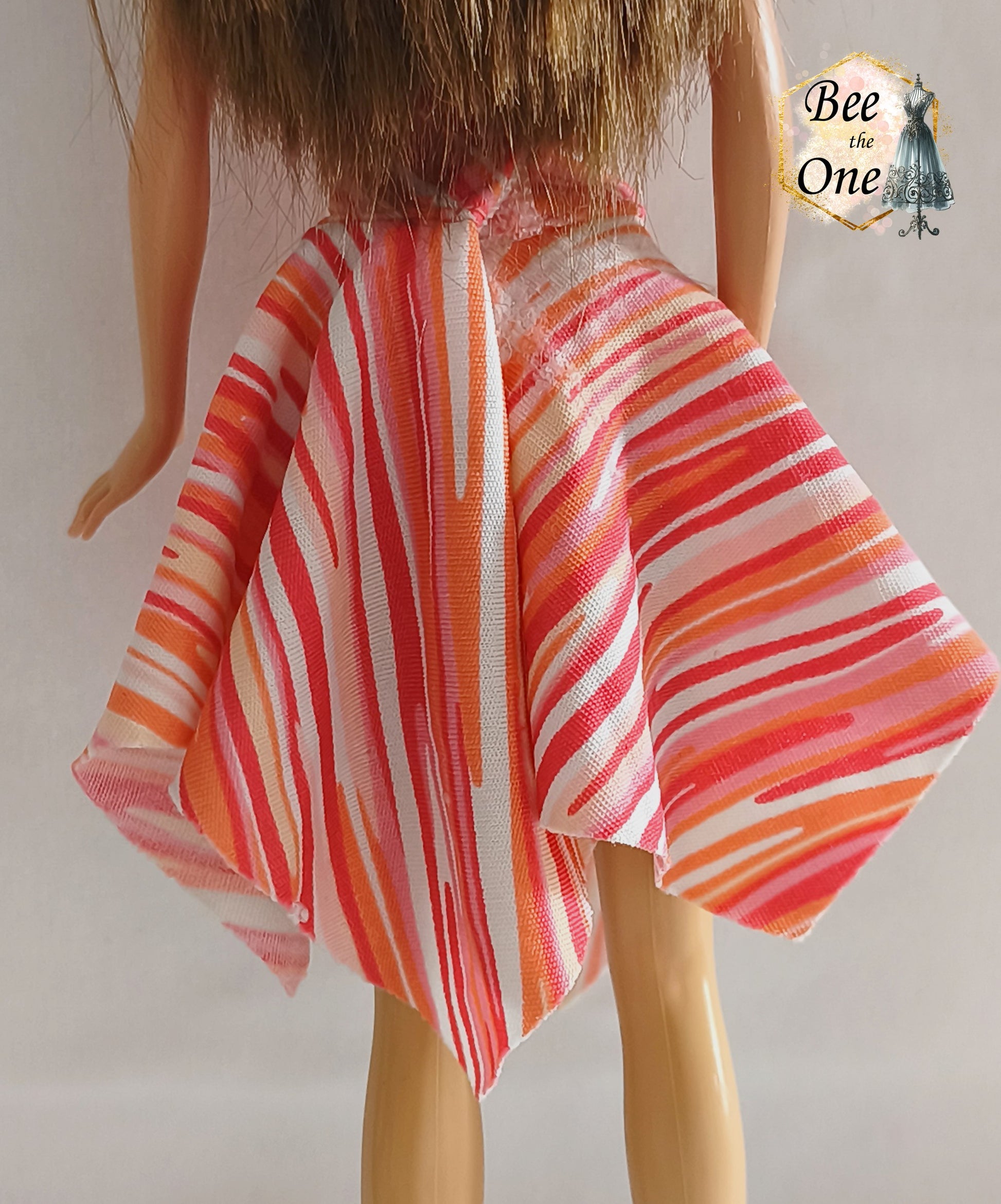 Robe asymétrique pour poupée mannequin Barbie Fashion Fever 2005, dos-nu à motifs géométriques corail, rose et orange avec attache argentée, présenté sur mannequin et fond blanc. Gros plan dos de la jupe