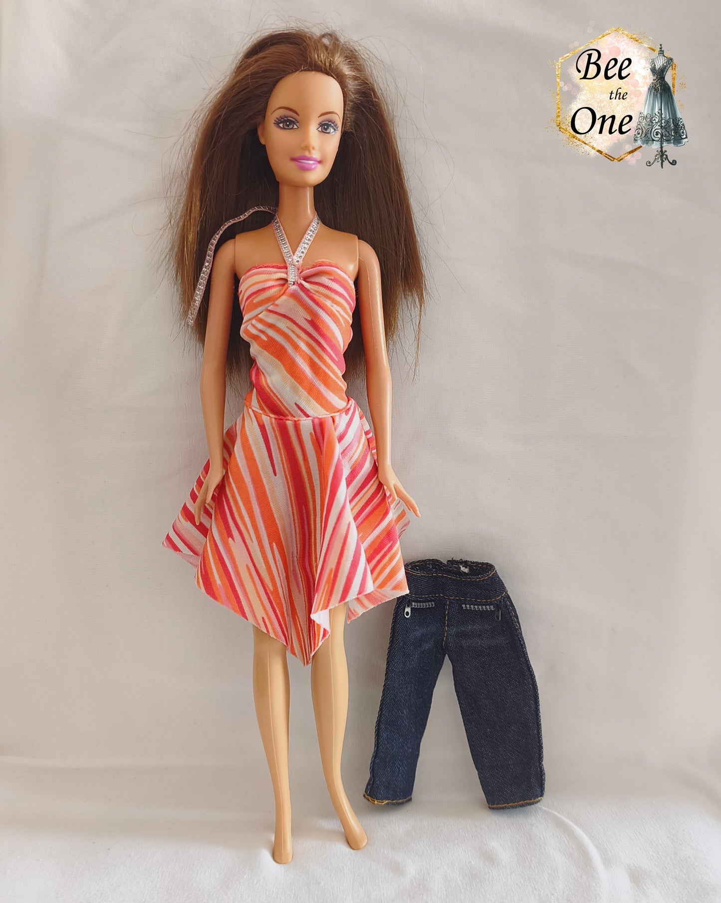 Ensemble de vêtements vintage pour poupée mannequin Barbie Fashion Fever 2005, composé d'une robe asymétrique dos-nu à motifs géométriques corail, rose et orange avec attache argentée, et d'un pantalon en jean denim brut avec faux zips, présenté sur mannequin et fond blanc.