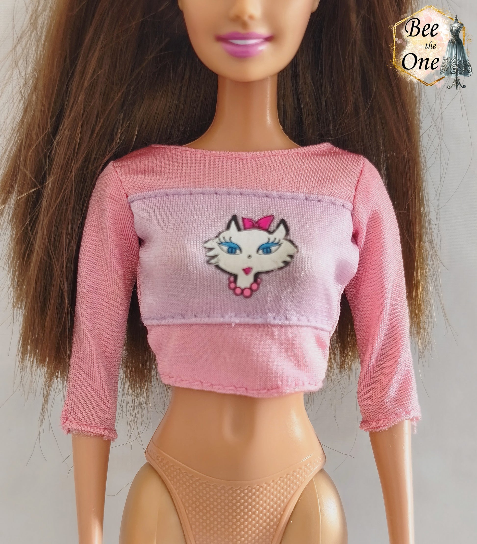 Top court rose à manches trois-quarts avec empiècement lilas orné d'un motif de tête de chat blanc, vêtement d'origine pour poupée Barbie Kitty Fun 2001, porté par une poupée brune sur fond blanc. Gros plan devant