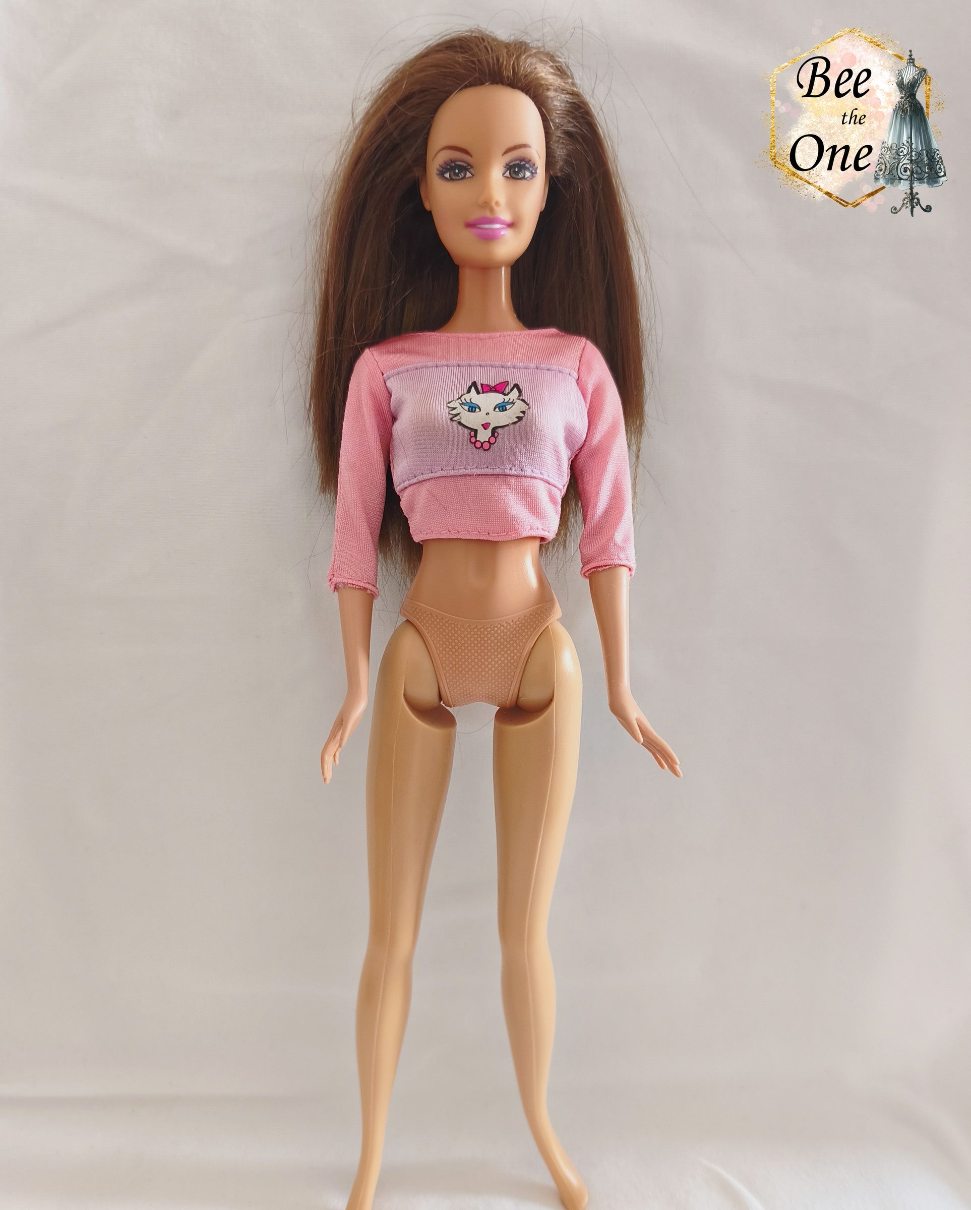 Top court rose à manches trois-quarts avec empiècement lilas orné d'un motif de tête de chat blanc, vêtement d'origine pour poupée Barbie Kitty Fun 2001, porté par une poupée brune sur fond blanc.