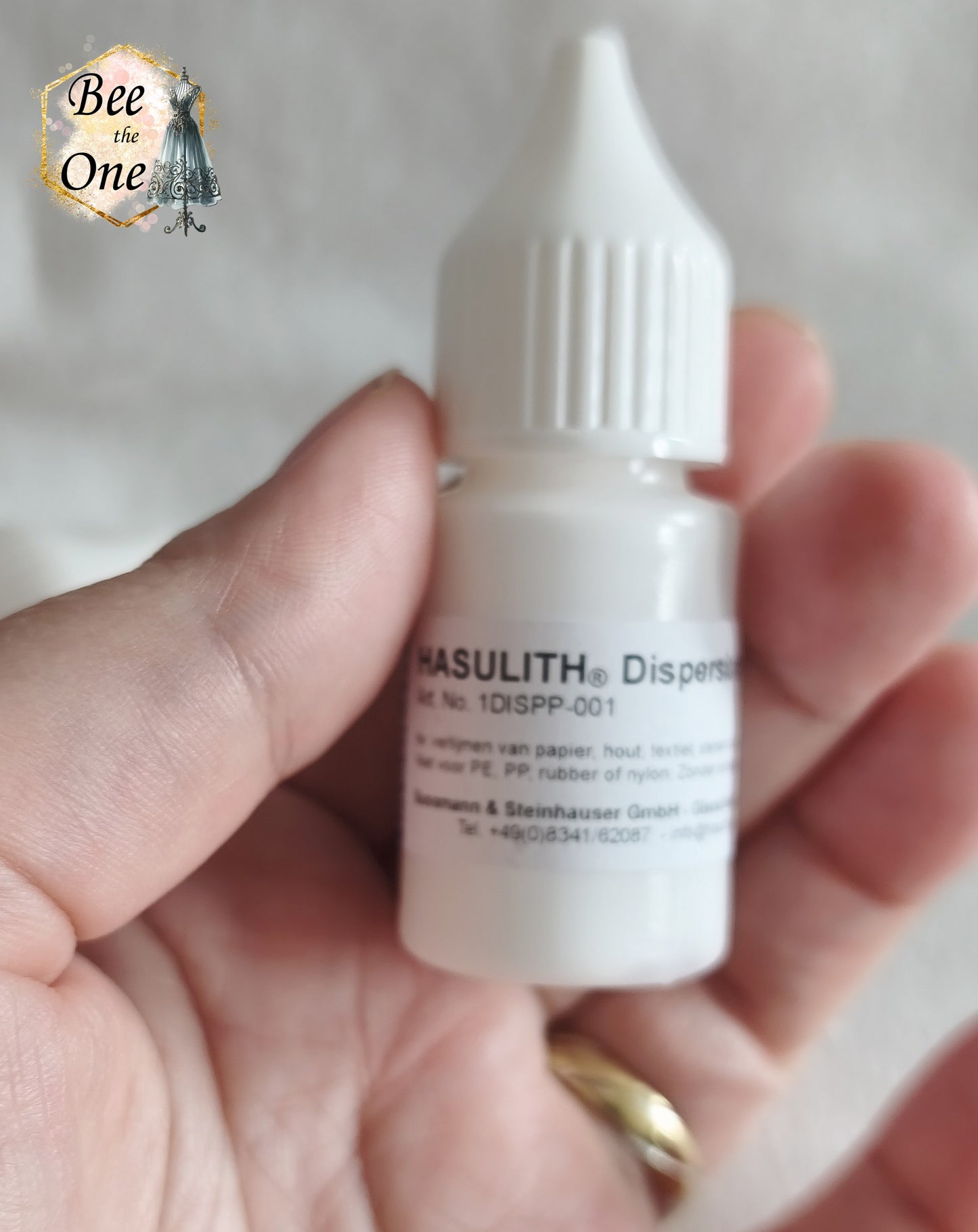 Flacon applicateur de colle Hasulith Dispersion de 10 ml avec bouchon blanc, sur un fond blanc texturé. Gros plan devant
