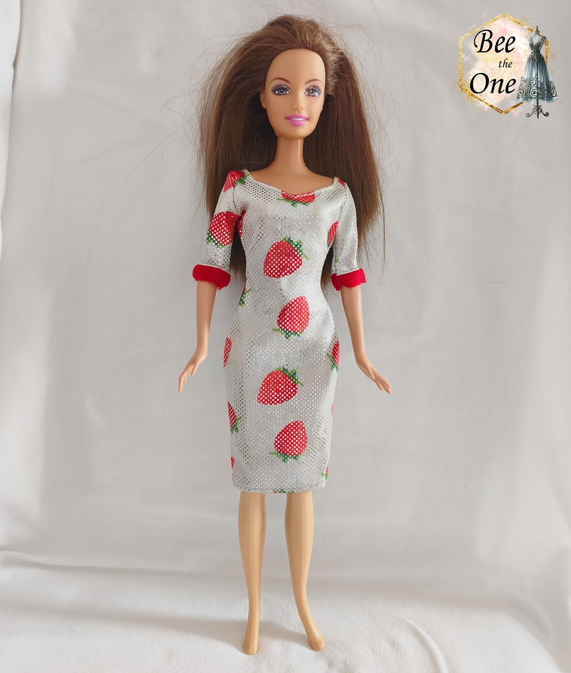 Robe mi-longue moulante argentée et scintillante à imprimé fraises rouges, avec bordures rouges douces aux manches, issue de la gamme Barbie Fashion Avenue 2002 de Mattel, portée par une poupée brune sur fond blanc