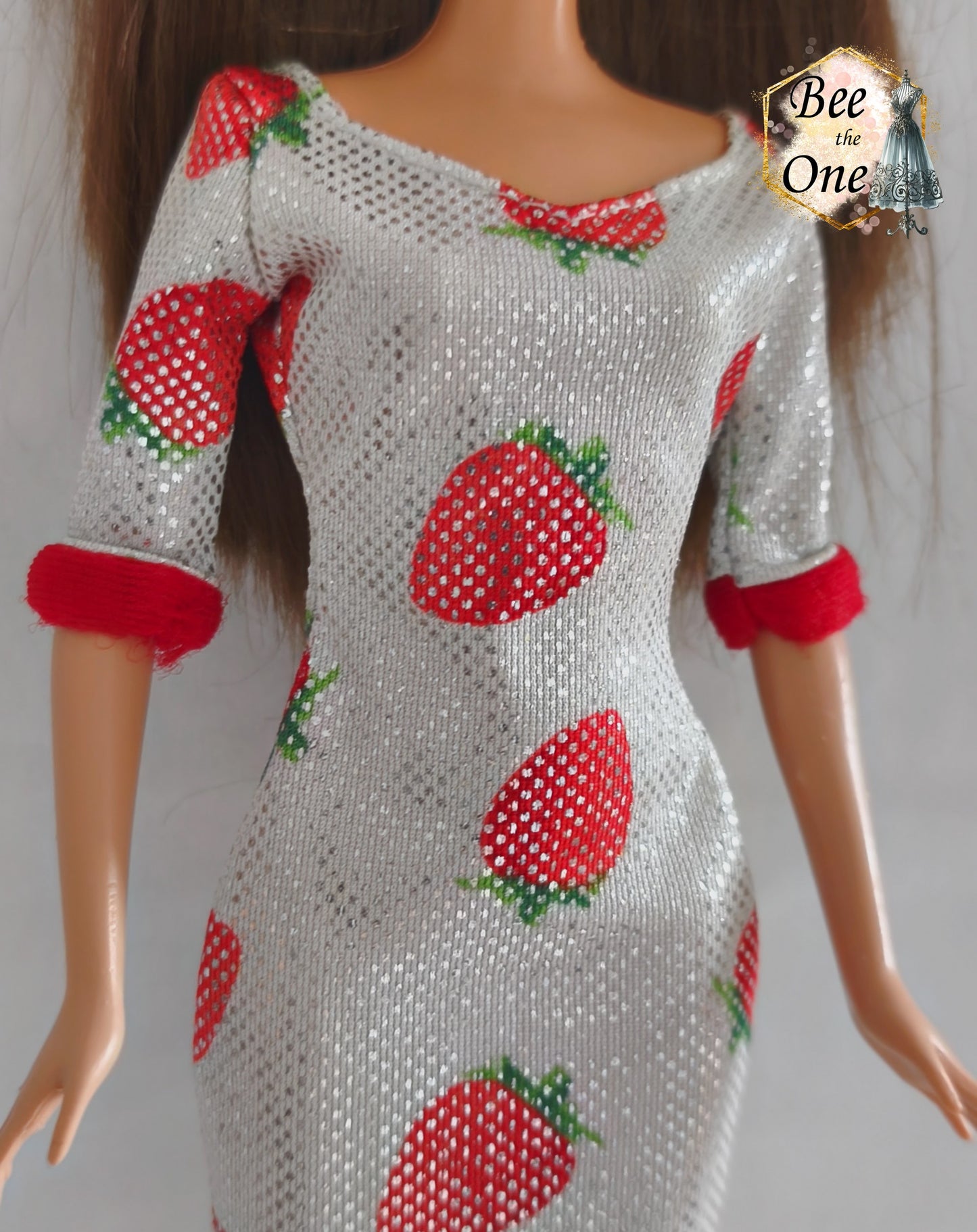 Robe mi-longue moulante argentée et scintillante à imprimé fraises rouges, avec bordures rouges douces aux manches, issue de la gamme Barbie Fashion Avenue 2002 de Mattel, portée par une poupée brune sur fond blanc. Gros plan devant