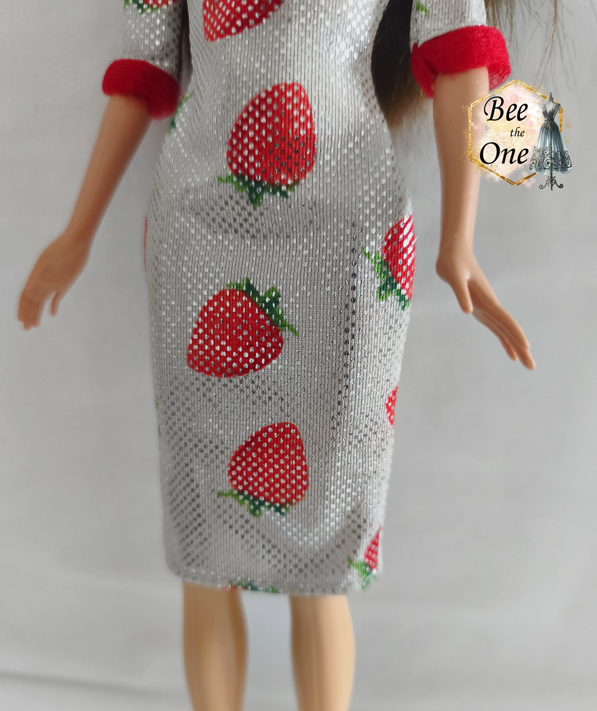 Robe mi-longue moulante argentée et scintillante à imprimé fraises rouges, avec bordures rouges douces aux manches, issue de la gamme Barbie Fashion Avenue 2002 de Mattel, portée par une poupée brune sur fond blanc. Gros plan bas devant