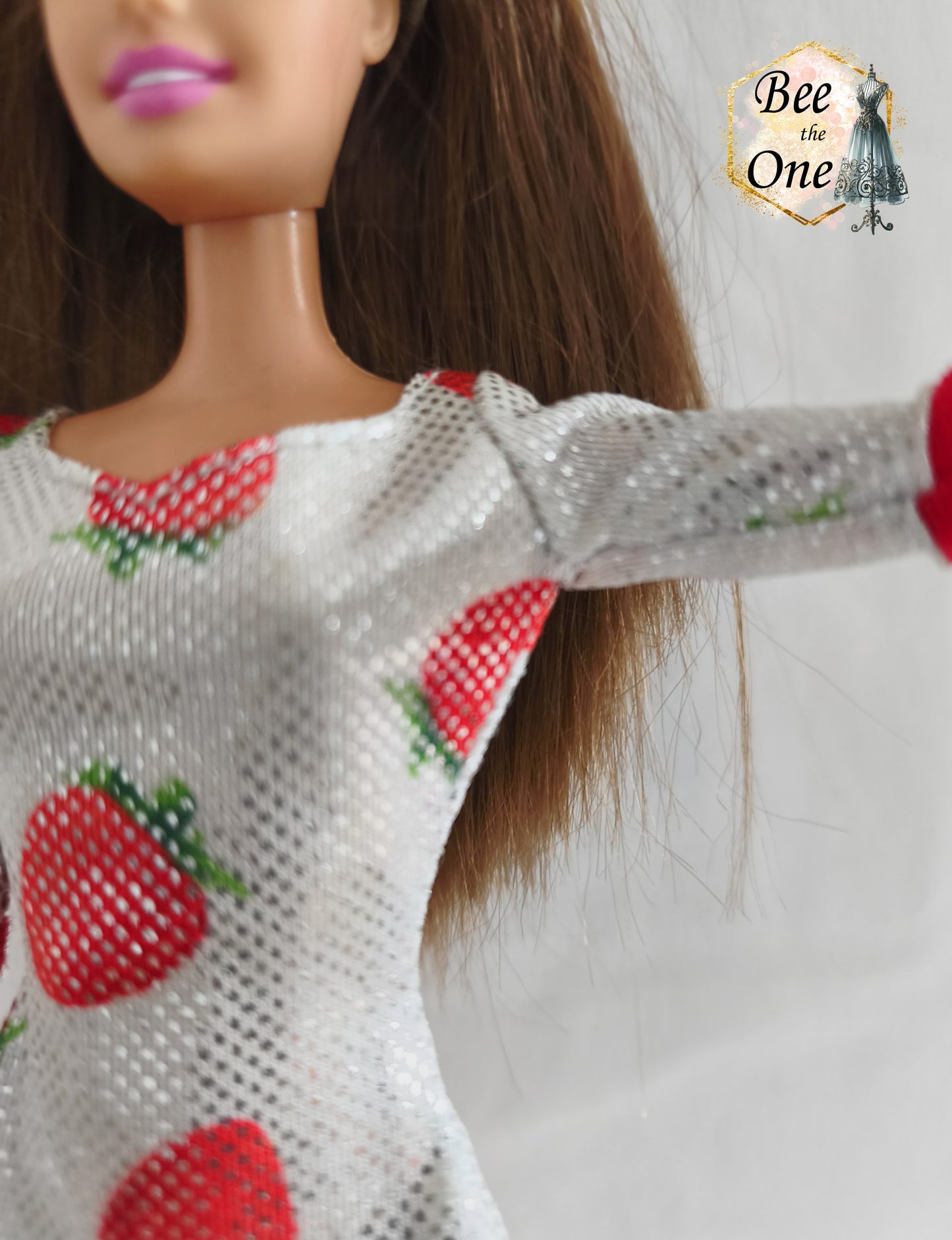 Robe mi-longue moulante argentée et scintillante à imprimé fraises rouges, avec bordures rouges douces aux manches, issue de la gamme Barbie Fashion Avenue 2002 de Mattel, portée par une poupée brune sur fond blanc. Gros plan manche gauche
