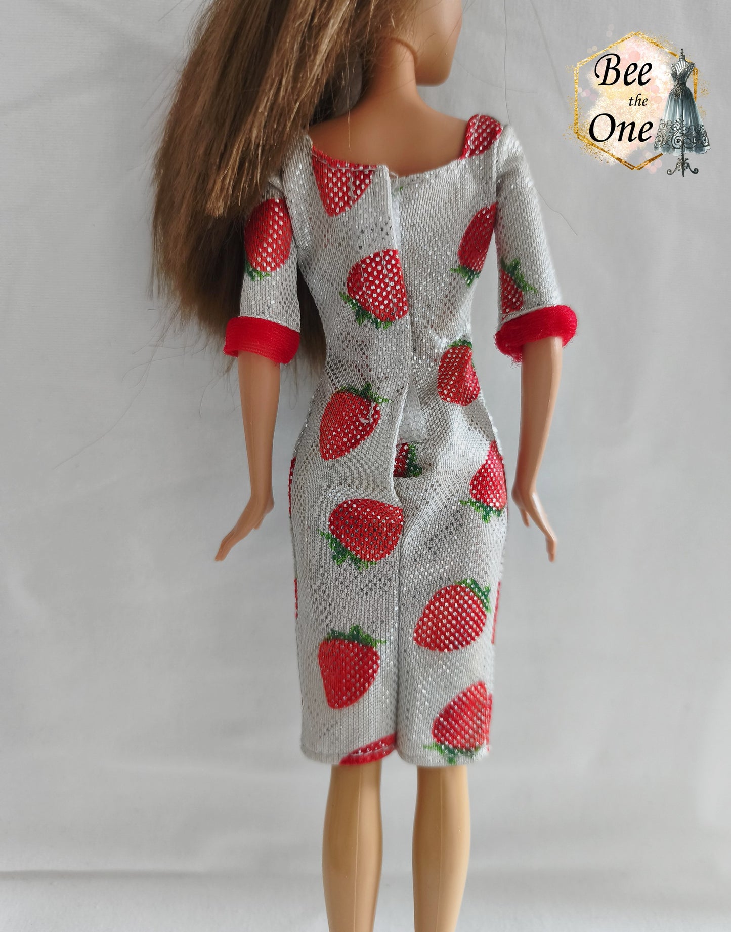 Robe mi-longue moulante argentée et scintillante à imprimé fraises rouges, avec bordures rouges douces aux manches, issue de la gamme Barbie Fashion Avenue 2002 de Mattel, portée par une poupée brune sur fond blanc. Gros plan dos