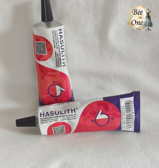 Un tube de colle Hasulith classique de 30 ml (27g) dans son emballage d'originerouge, violet et blanc, posé sur un fond blanc texturé