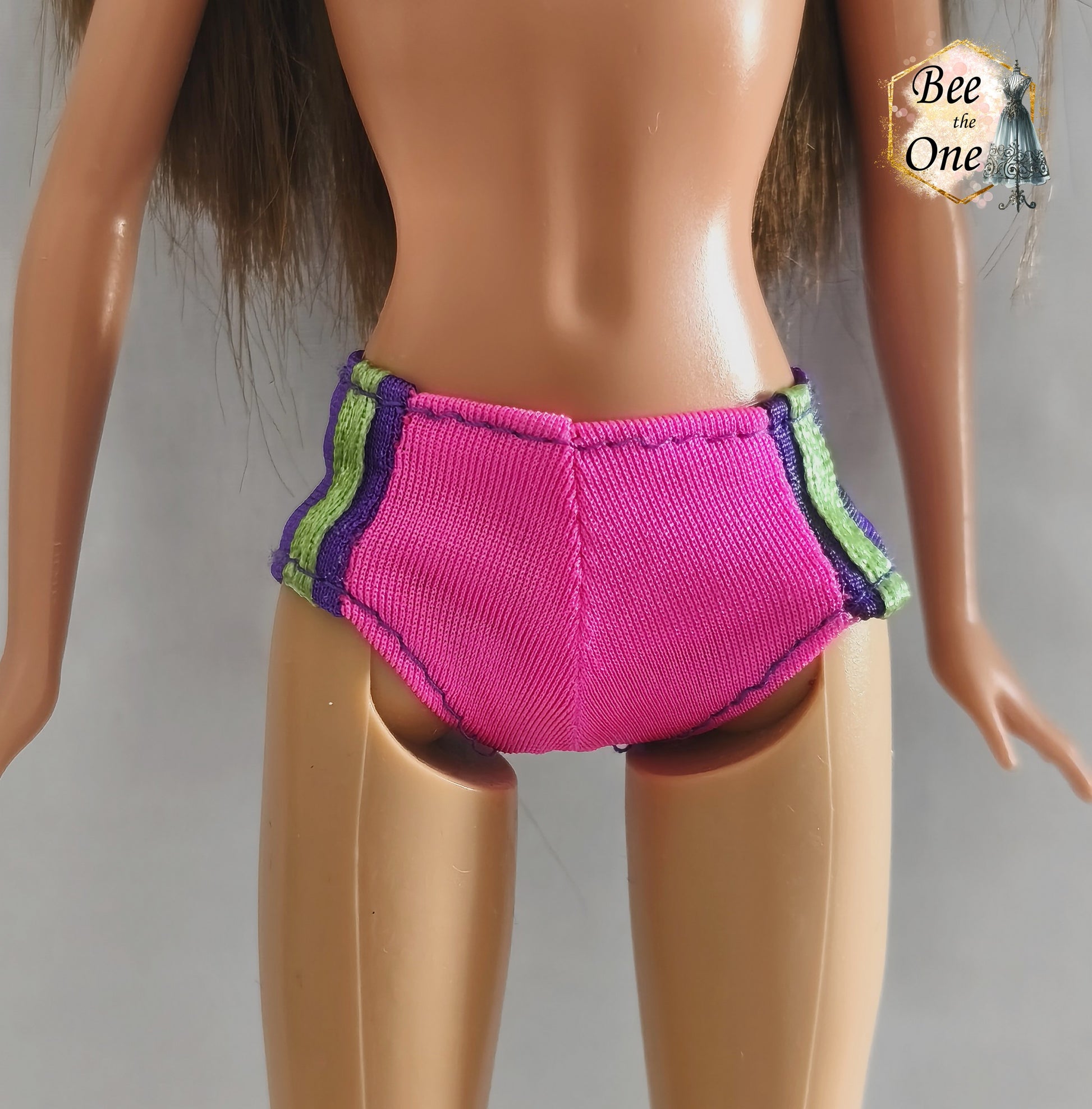 Culotte de maillot de bain rose fuchsia avec rayures latérales vert fluo et violettes, vêtement d'origine pour poupée Barbie Surf City 2000, portée par une poupée brune sur fond blanc. Gros plan devant