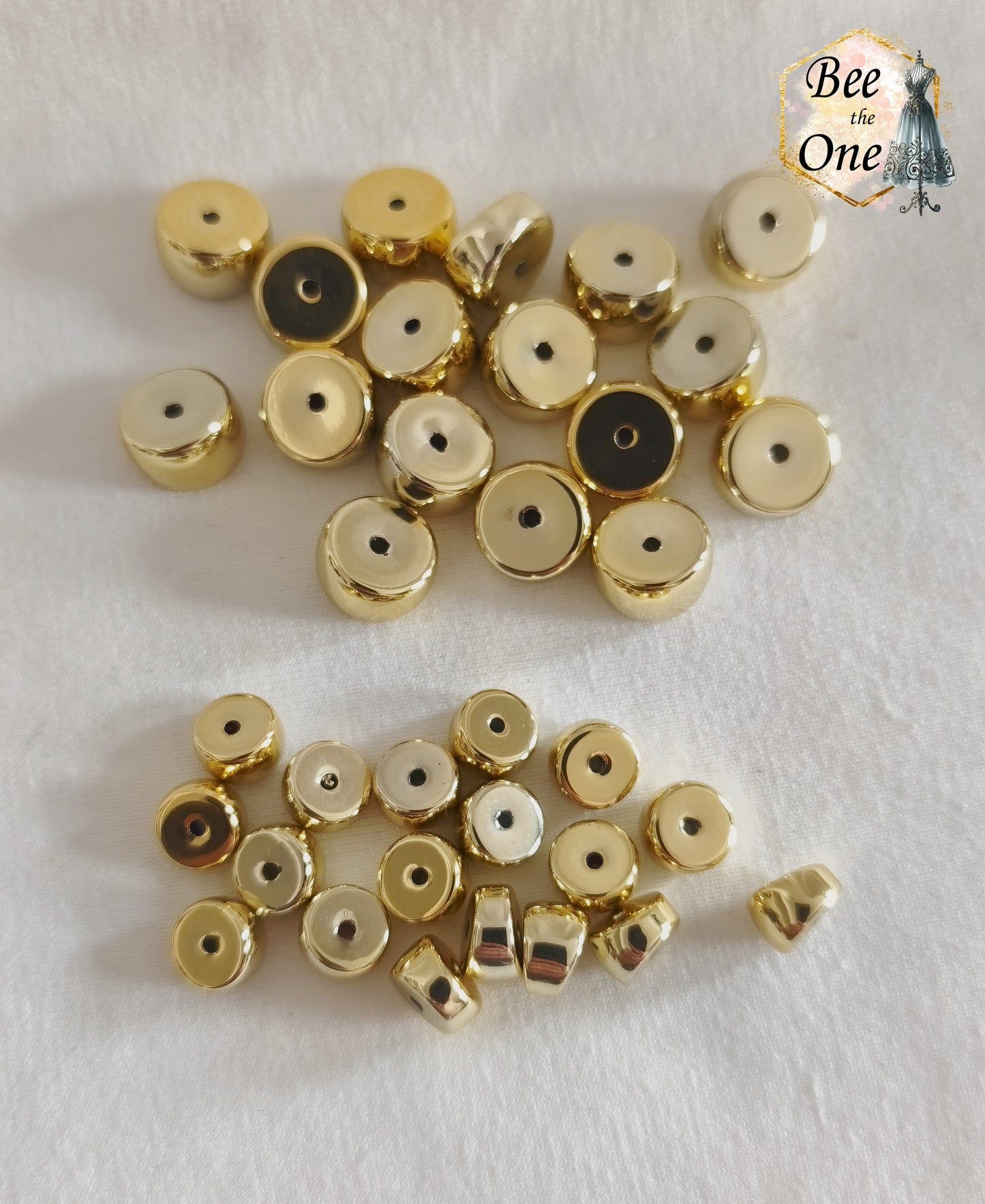 Perles tubes séparateurs incurvées en acrylique doré avec finition métallisée brillante et effet miroir, mesurant 11 mm, disposées sur un fond blanc texturé. Gros plan d'une perle entre deux doigts. Comparaison avec un lot de diamètre 8 mm