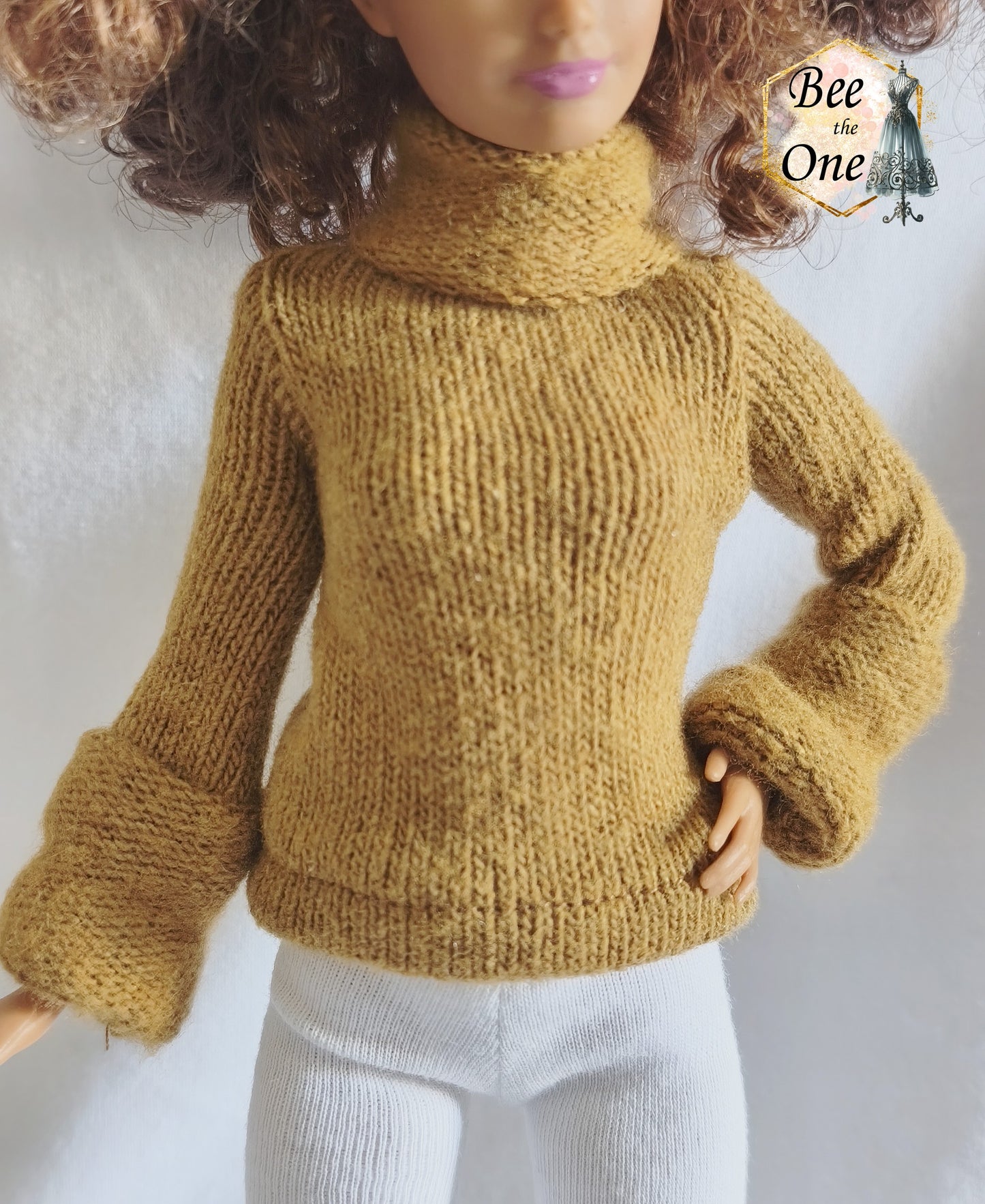 Pull à col roulé fait main en maille fine couleur marron argile, création artisanale ajustée spécialement pour poupée Barbie morphologie Petite, porté avec un legging blanc sur fond blanc. gros plan devant