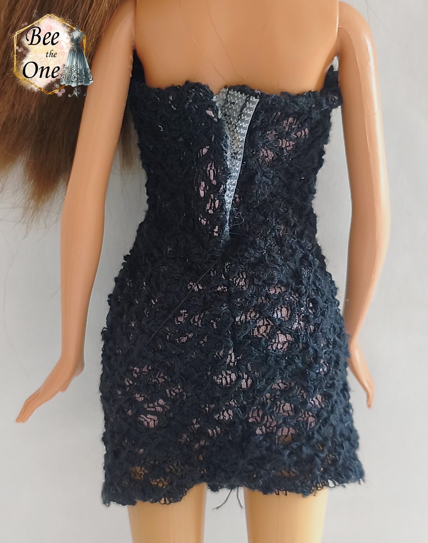 Robe bustier courte pour poupée Barbie en dentelle noire sur doublure rose, ornée sous la poitrine d'un ruban satiné rose et d'une fleur textile avec perle au centre, issue de la gamme Fashion Fever 2005 de Mattel, portée sur fond blanc. gros plan de dos