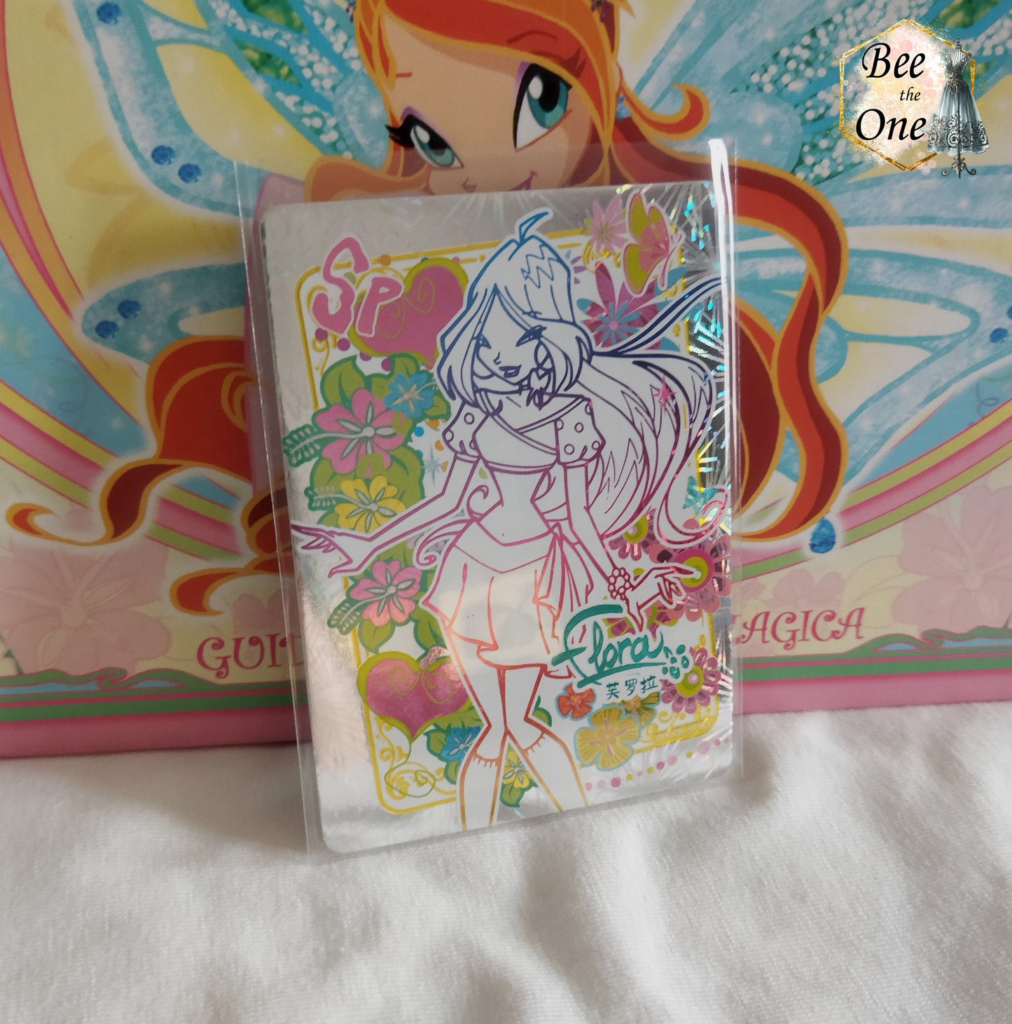 Carte de collection Winx Club brillante type hologramme représentant la fée Flora, édition spéciale SP avec illustrations de fleurs exotiques et cœurs colorés.