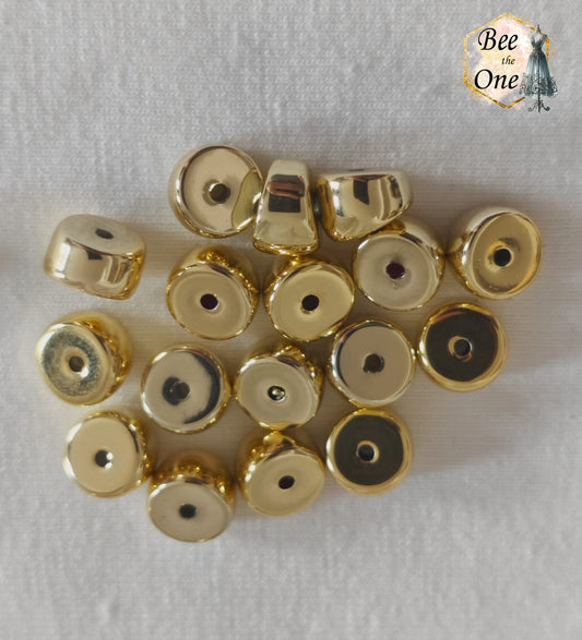 Perles tubes séparateurs incurvées en acrylique doré avec finition métallisée brillante et effet miroir, mesurant 11 mm, disposées sur un fond blanc texturé