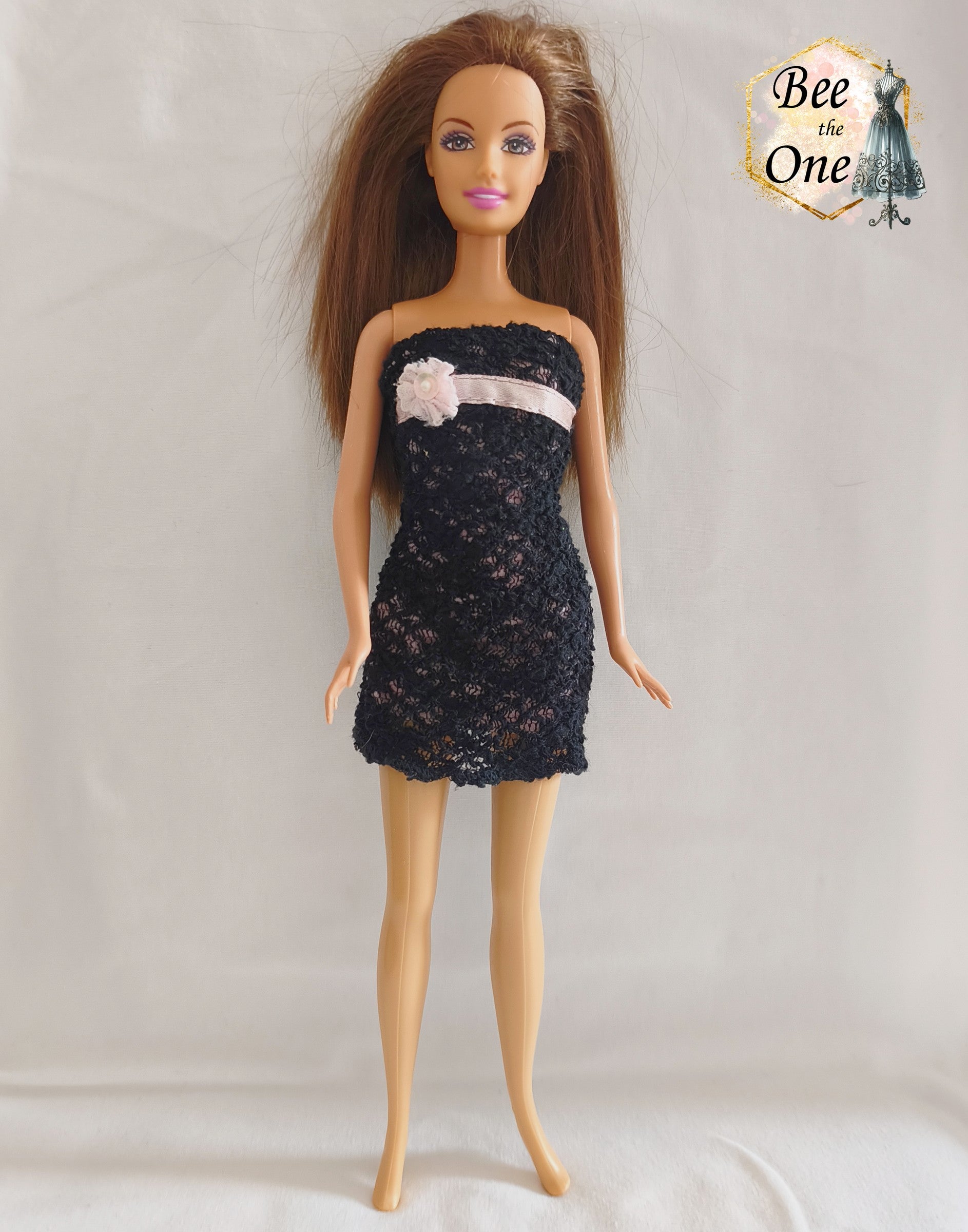 Robe bustier courte pour poupée Barbie en dentelle noire sur doublure rose, ornée sous la poitrine d'un ruban satiné rose et d'une fleur textile avec perle au centre, issue de la gamme Fashion Fever 2005 de Mattel, portée sur fond blanc.