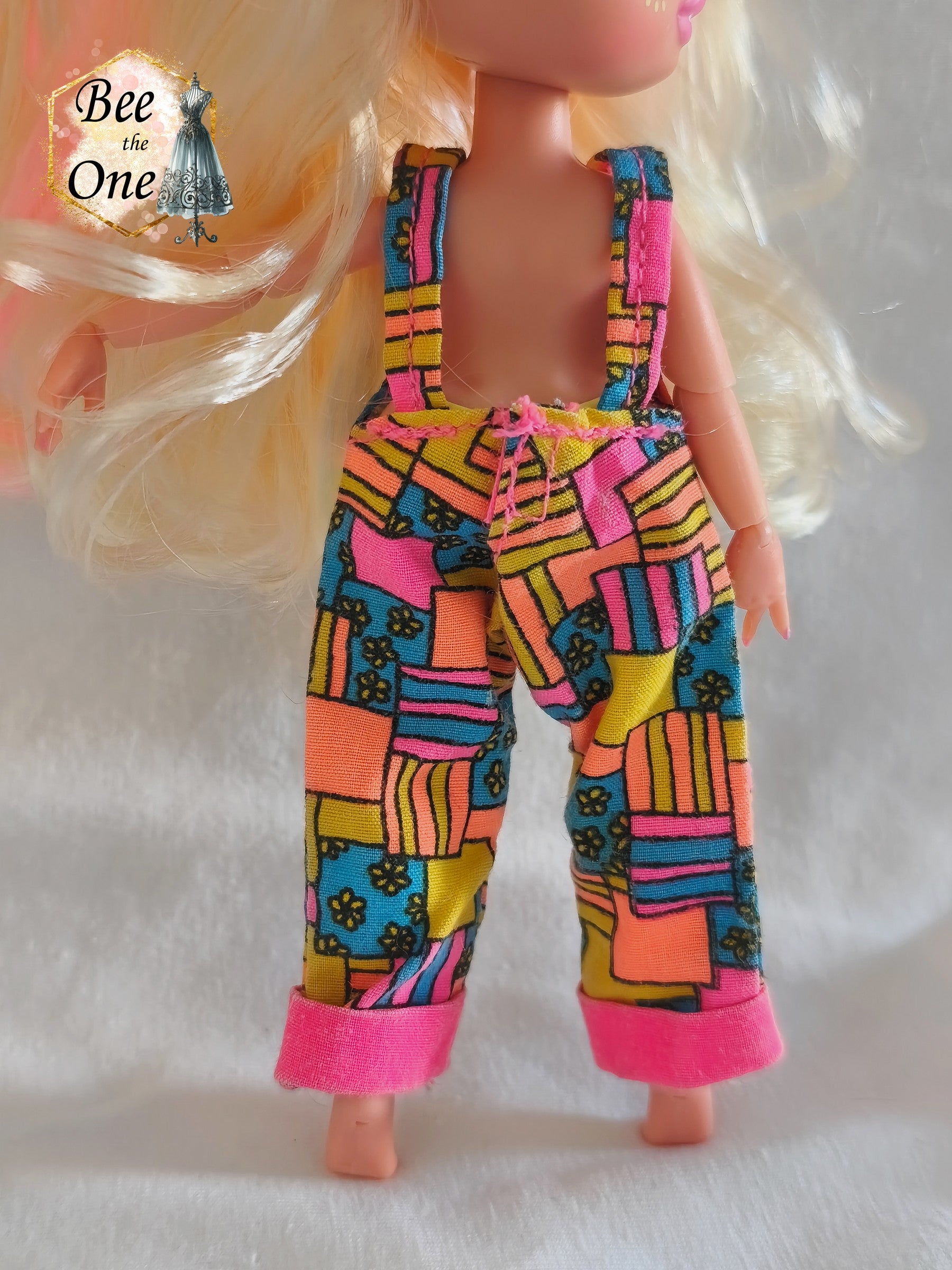 Salopette vintage Sindy & Cyclin Sam Hasbro 1996 à motifs patchwork colorés (rose, orange, jaune, bleu), portée par une poupée LOL OMG Tween sur fond blanc. Gros plan dos