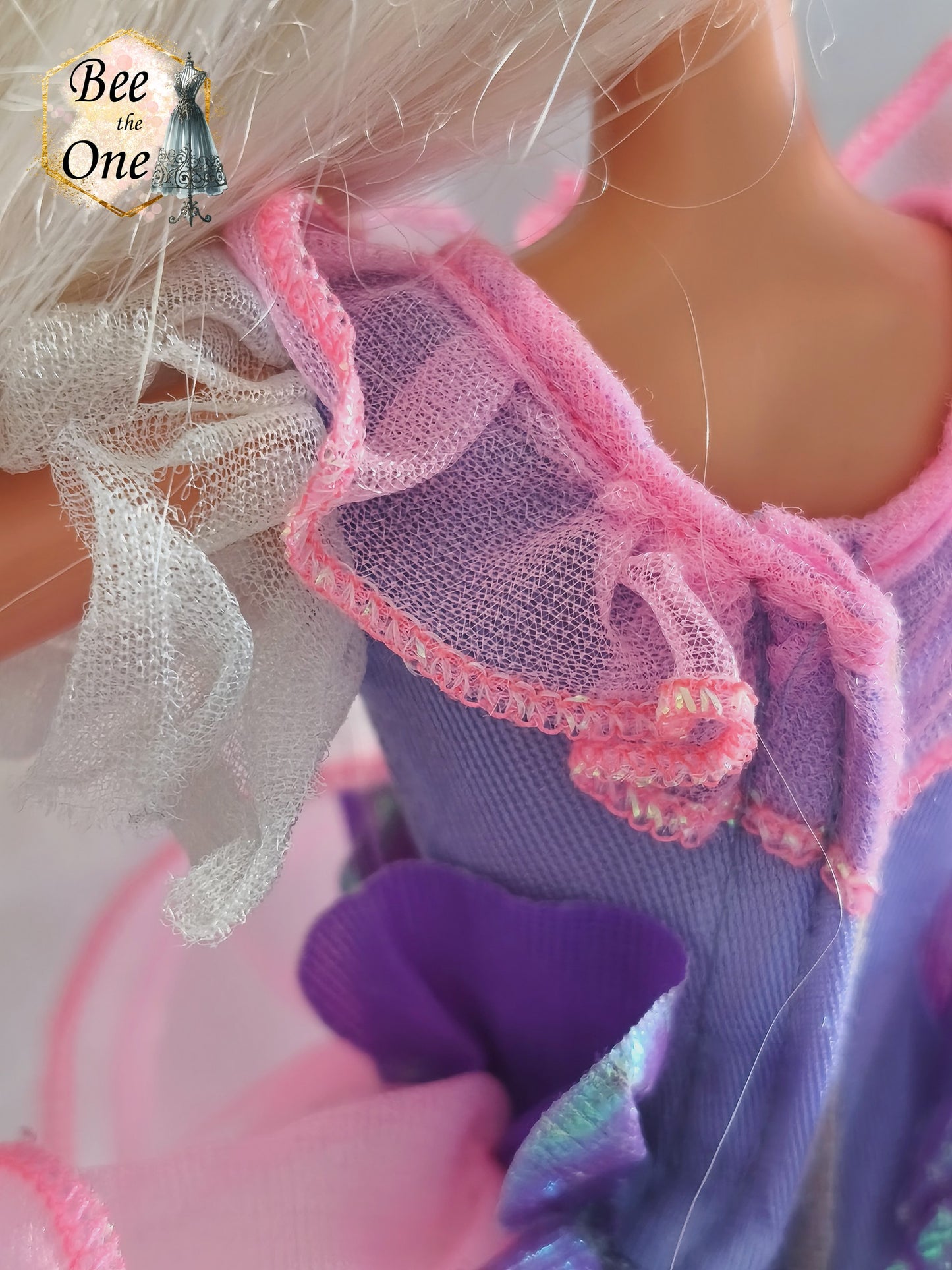 Robe de poupée Barbie Toothfairy 1994, édition spéciale exclusive Walmart, portée par une poupée blonde sur fond blanc. Le body est mauve et le tutu rose. À noter : les parties blanches en tulle sur les manches et sous le tutu sont très déchirées et endommagées. Gros plan encolure gauche