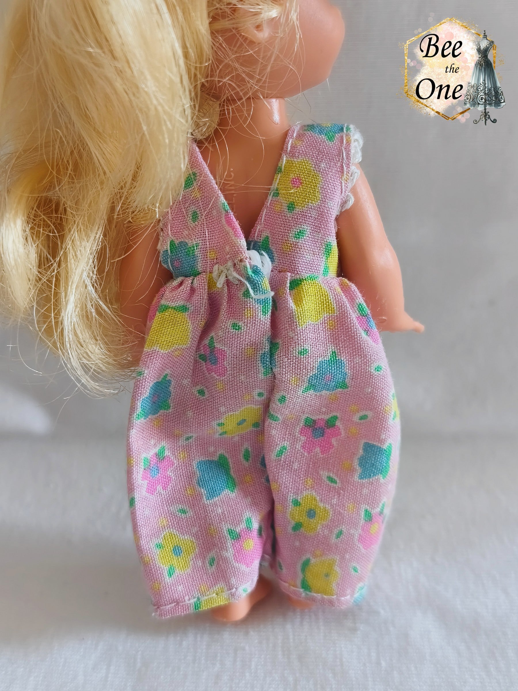 Combinaison salopette rose à motifs de petites fleurs multicolores (bleu, jaune, vert, rose) pour poupée Shelly (Kelly), issue du coffret Barbie Dentiste 1997 de Mattel, portée par une petite poupée blonde sur fond blanc. gros plan dos