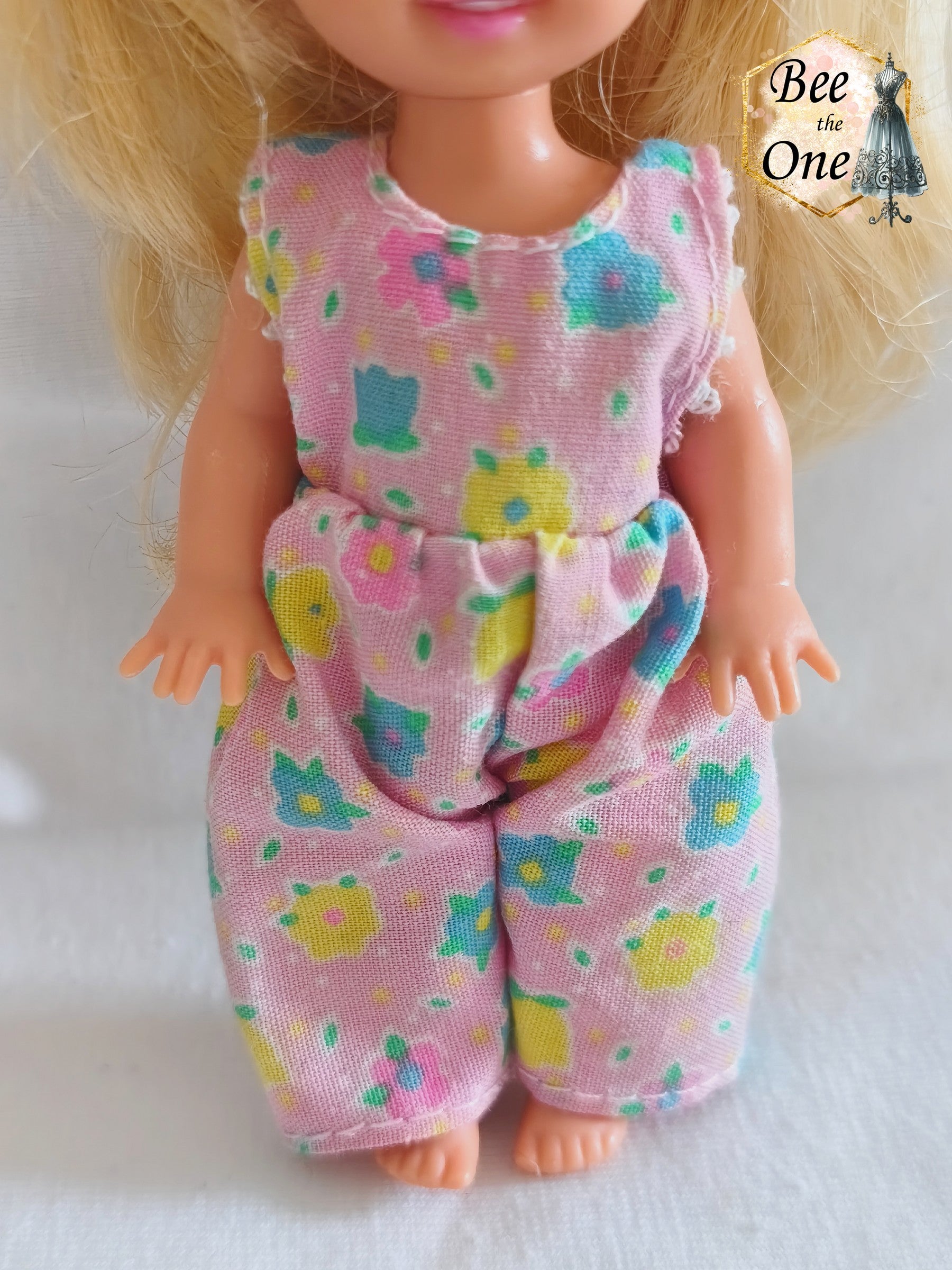 Combinaison salopette rose à motifs de petites fleurs multicolores (bleu, jaune, vert, rose) pour poupée Shelly (Kelly), issue du coffret Barbie Dentiste 1997 de Mattel, portée par une petite poupée blonde sur fond blanc. gros plan devant