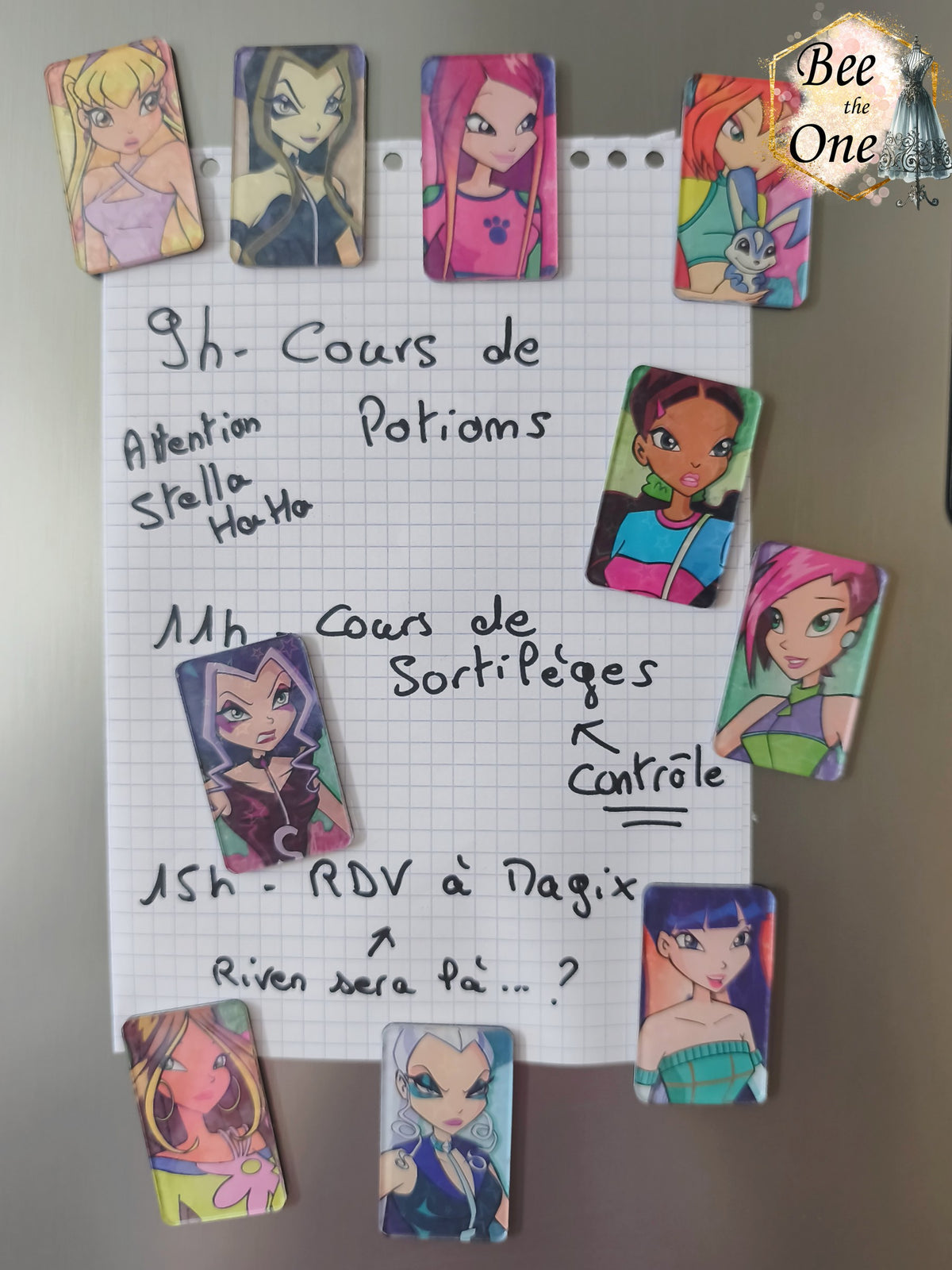 Magnets décoratifs rectangulaires plats mettant en scène les personnages du dessin animé Winx Club et les Trix (Bloom, Stella, Flora, Layla, Musa, Tecna, Roxy, Icy, Darcy, Stormy), disposés sur une surface métallique grise. Les magnets fixent une feuille de papier sur la surface métallique