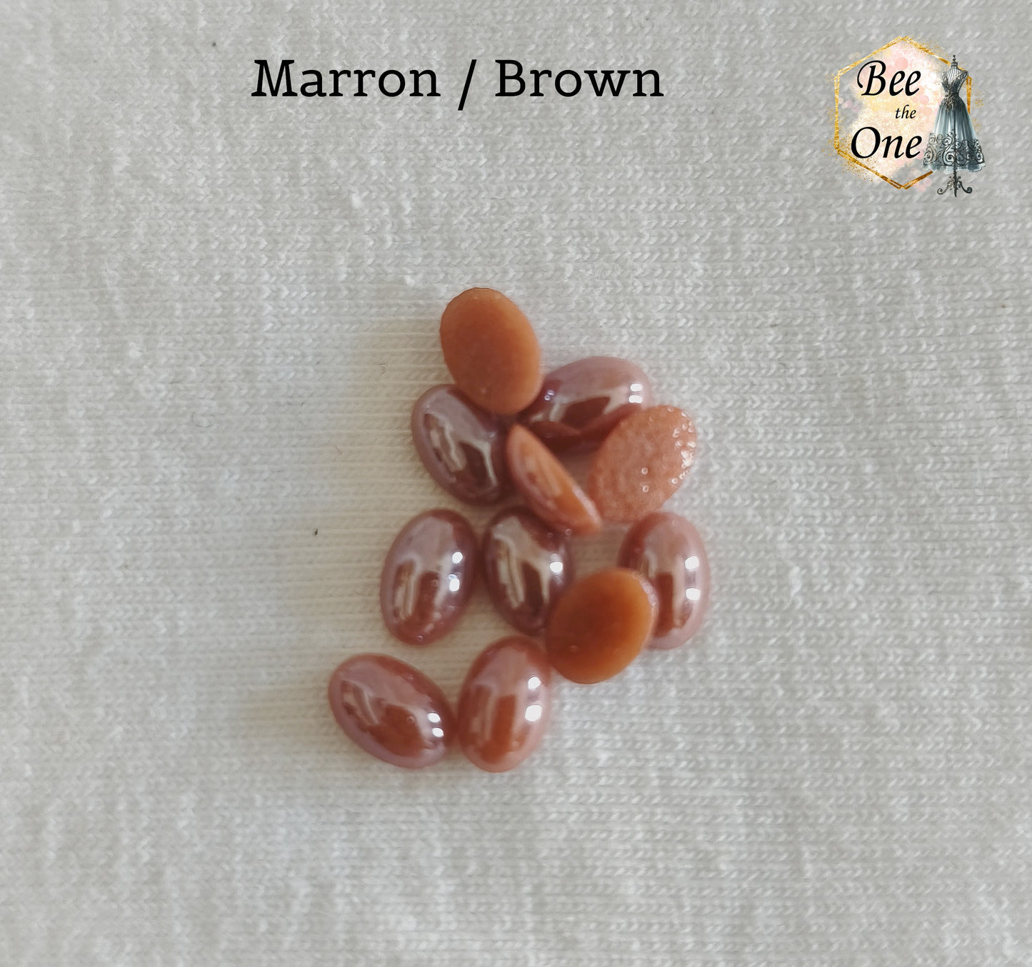 Mini cabochons ovales lisses de 6x4 mm en acrylique marron, posés sur un fond blanc.