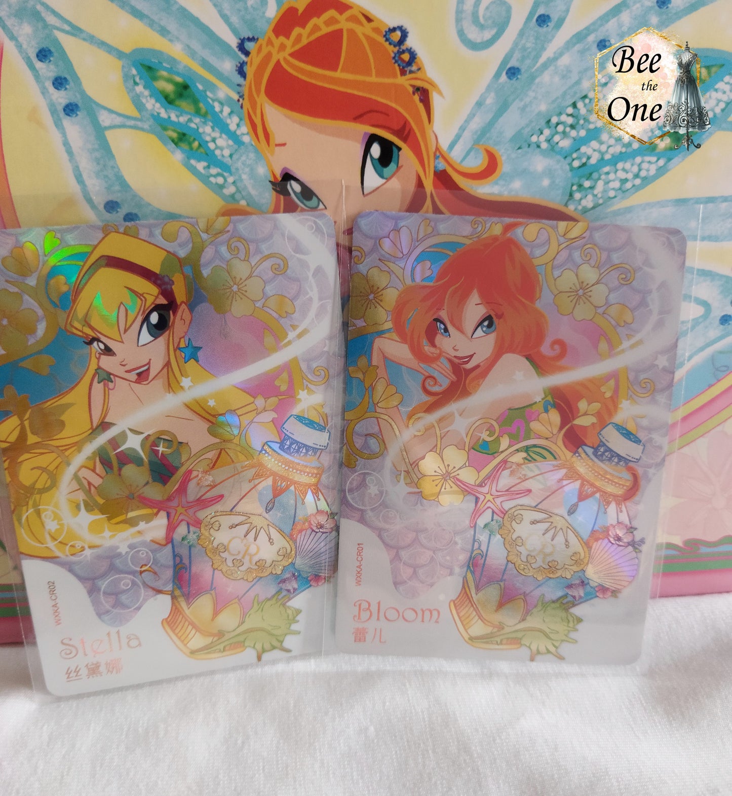 Cartes à collectionner inspirées de l'univers magique de Winx Club, mettant en scène Stella et Bloom dans un style coloré et féerique. Les cartes sont ornées de motifs floraux, potion et de détails étincelants, évoquant la magie et l'aventure.