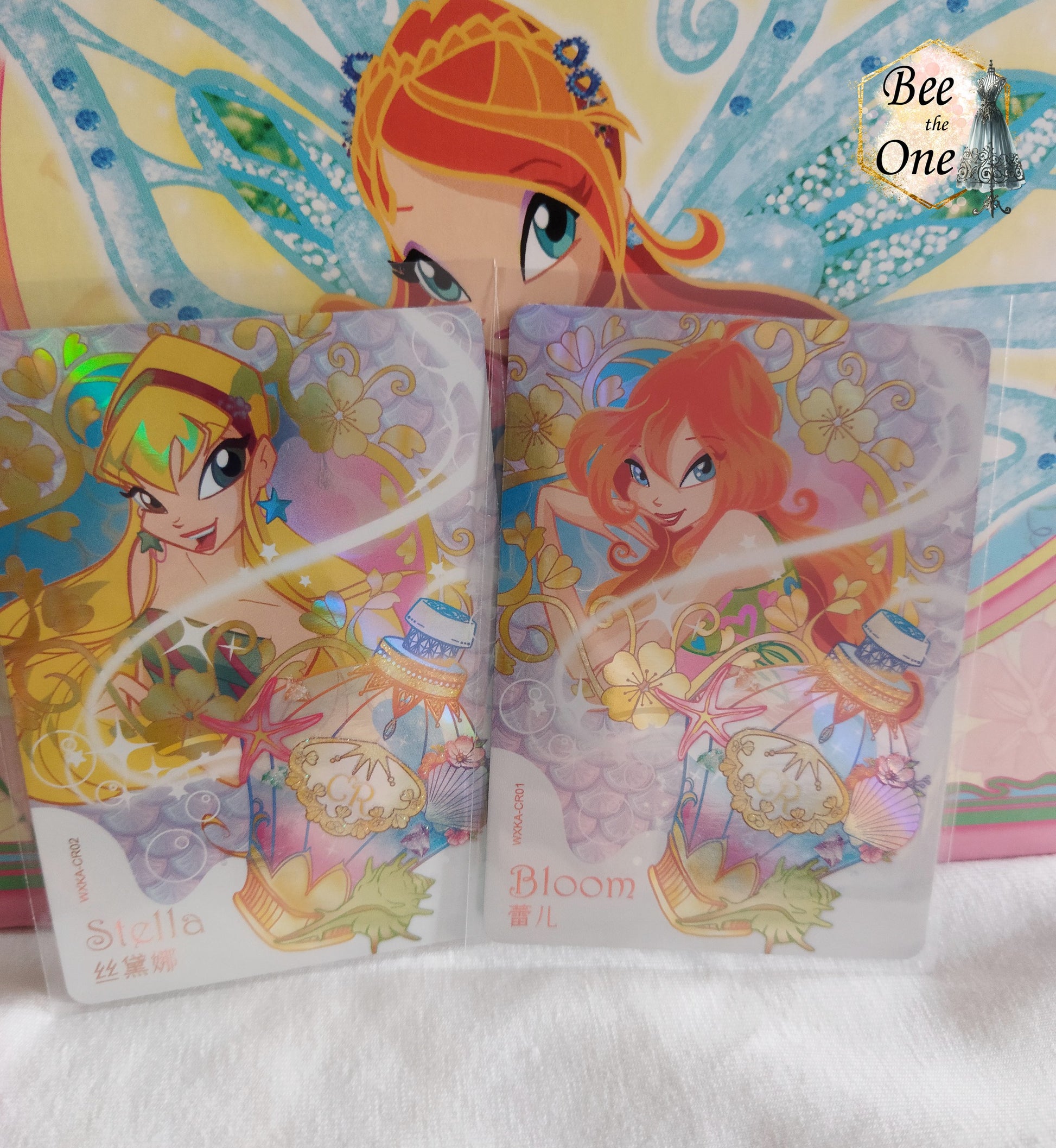 Cartes à collectionner inspirées de l'univers magique de Winx Club, mettant en scène Stella et Bloom dans un style coloré et féerique. Les cartes sont ornées de motifs floraux, potion et de détails étincelants, évoquant la magie et l'aventure.