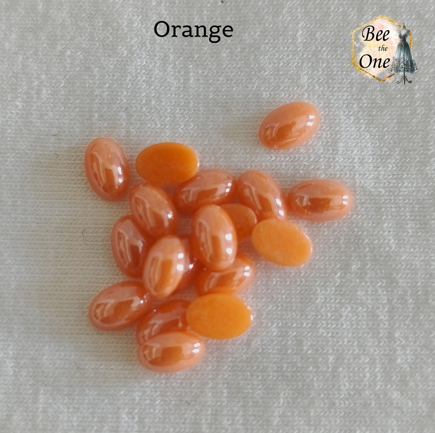 Mini cabochons ovales lisses de 6x4 mm en acrylique orange, posés sur un fond blanc.