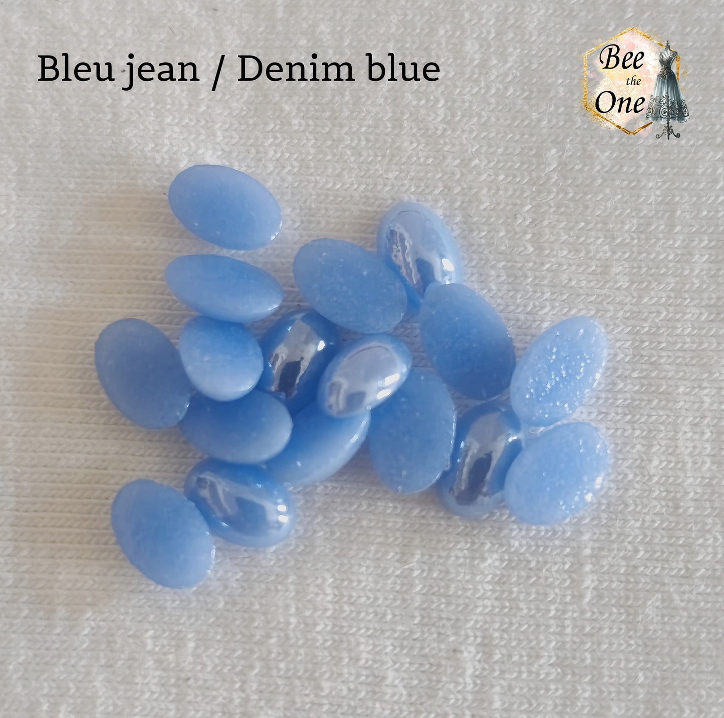 Mini cabochons ovales lisses de 6x4 mm en acrylique bleu jean, posés sur un fond blanc.