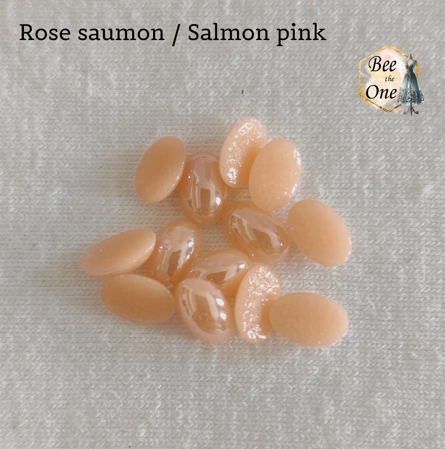 Mini cabochons ovales lisses de 6x4 mm en acrylique rose saumon, posés sur un fond blanc.