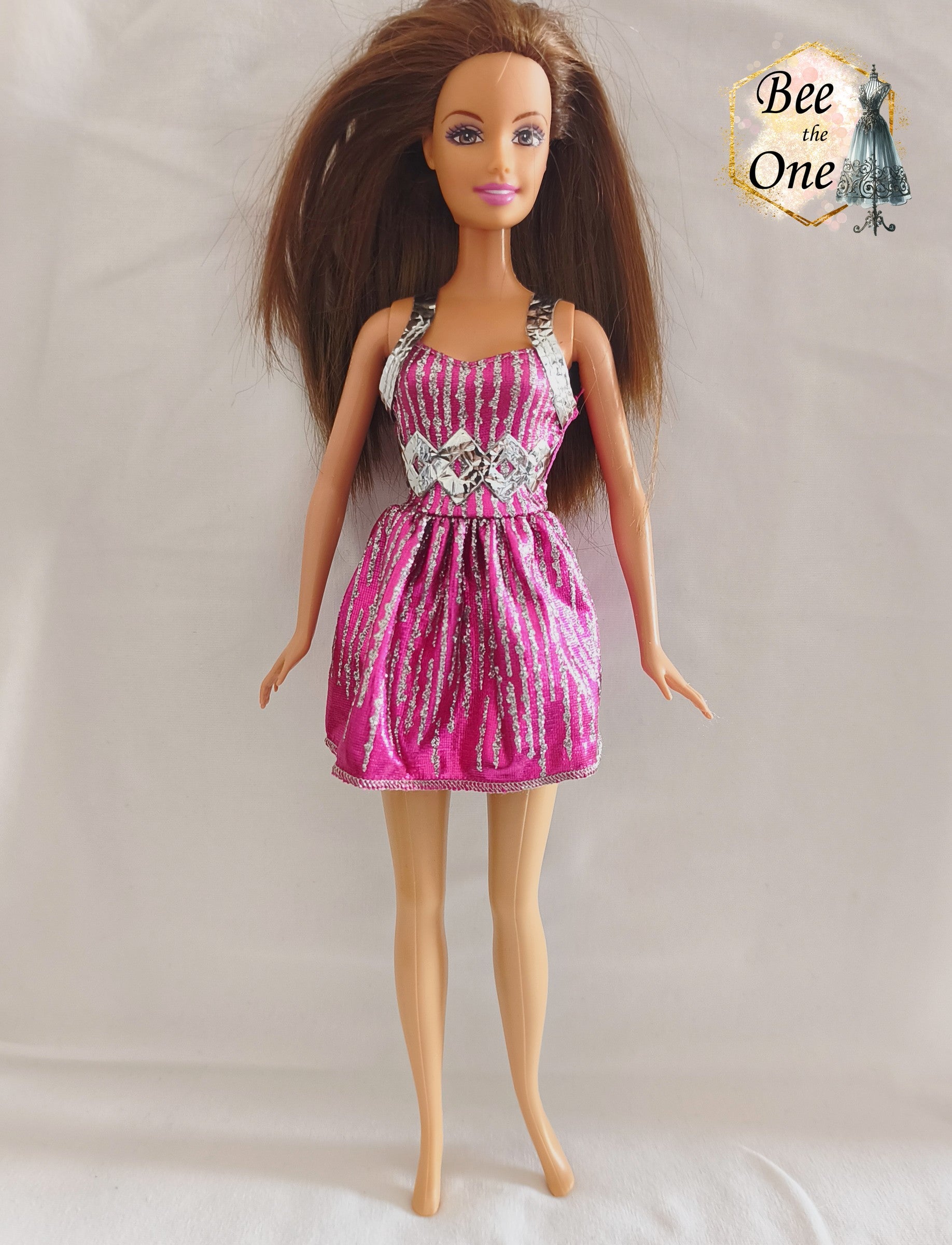 Robe courte de fête rose fuchsia brillante avec rayures verticales pailletées argentées, bretelles métallisées et découpes géométriques en losanges à la taille, vêtement d'origine pour poupée Barbie Fashionistas 2013, portée par une poupée brune sur fond blanc.