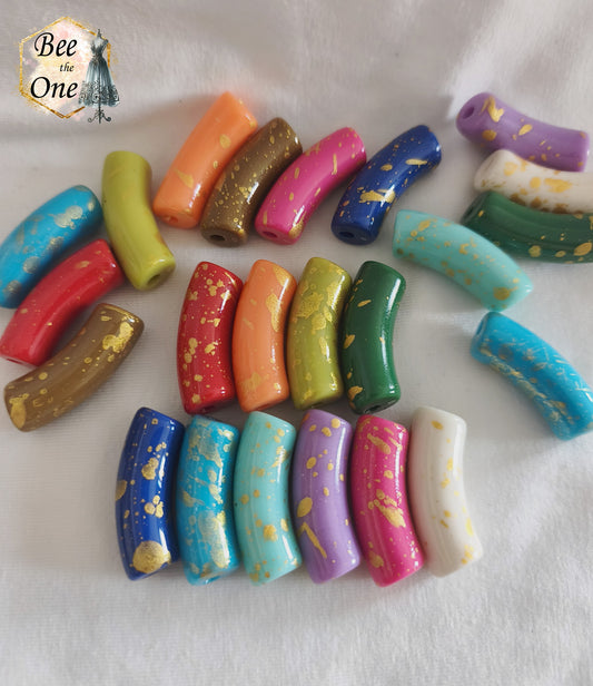 Assortiment de grandes perles tubes incurvées en acrylique mesurant 34x11 mm. Les perles sont multicolores (bleu, vert, rouge, rose, violet, orange, blanc) et ornées d'éclats et de mouchetures dorées, disposées sur un fond blanc.
