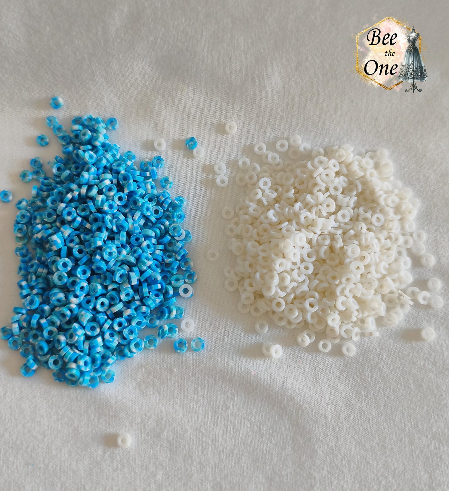 Petites perles rondelles Heishi Katsuki de 4 mm en pâte polymère, séparées en deux tas : à gauche des perles marbrées bleu turquoise et blanc, à droite des perles blanches, présentées sur tissu blanc.