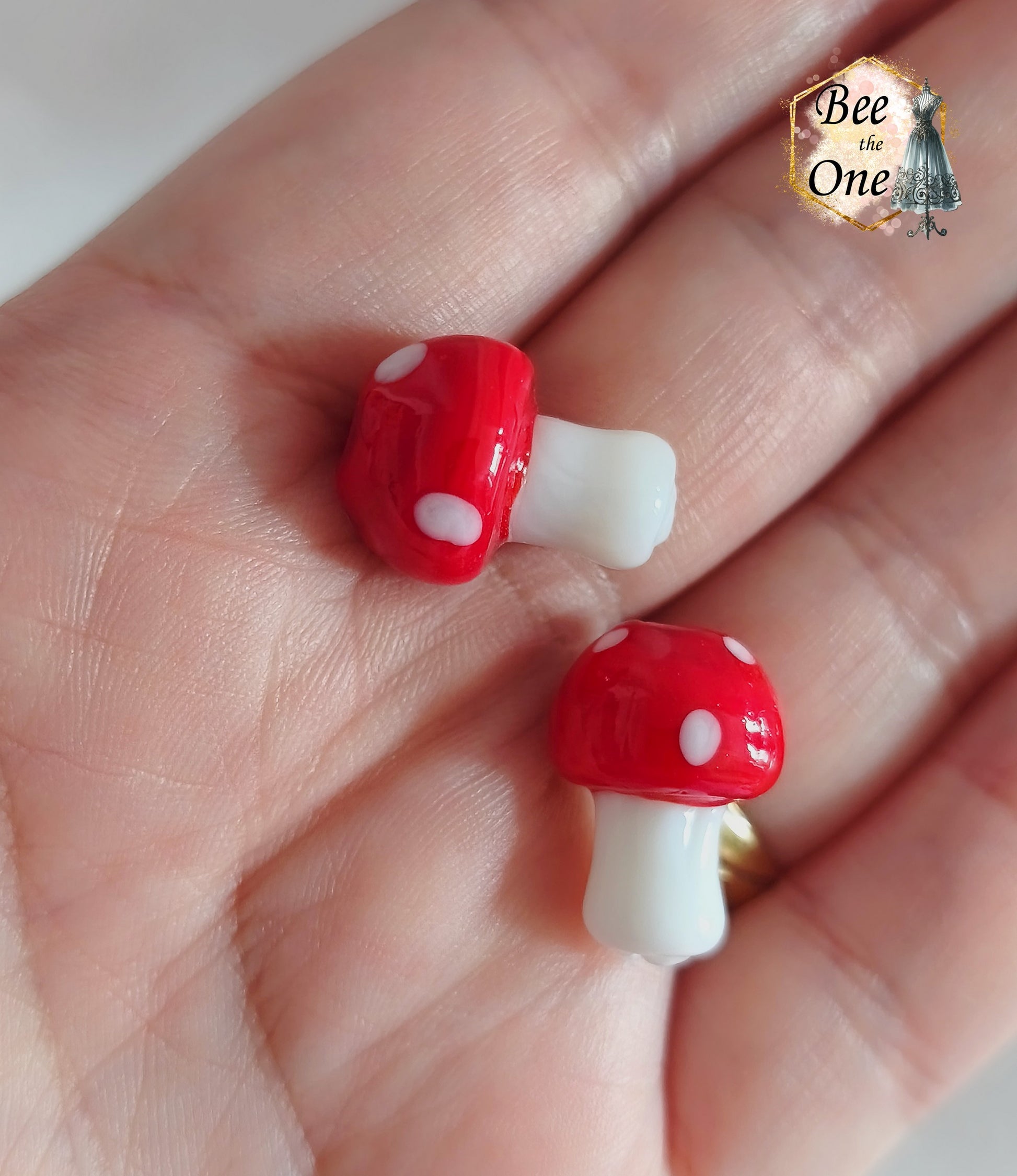 Perles en verre filé rouge et blanc en forme de champignon amanite tue-mouche à pois, percées verticalement, sur fond blanc. gros plan