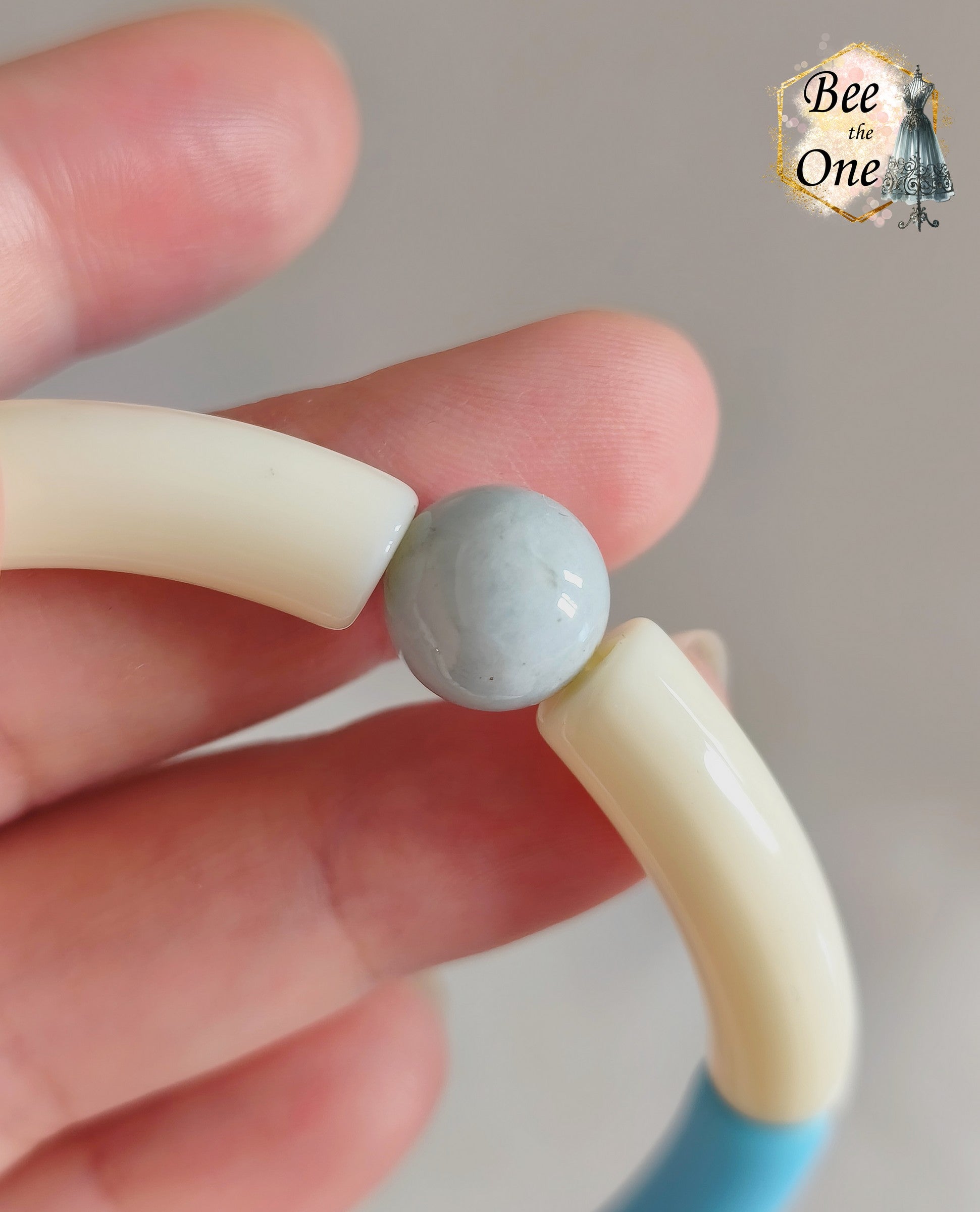 Set de trois bracelets élastiques faits main pour adulte, composés de perles tubes incurvées en acrylique aux teintes bleu azur, orange vif et crème, avec détails marbrés dorés et séparateurs dorés. Gros plan sur une perle en aigue marine