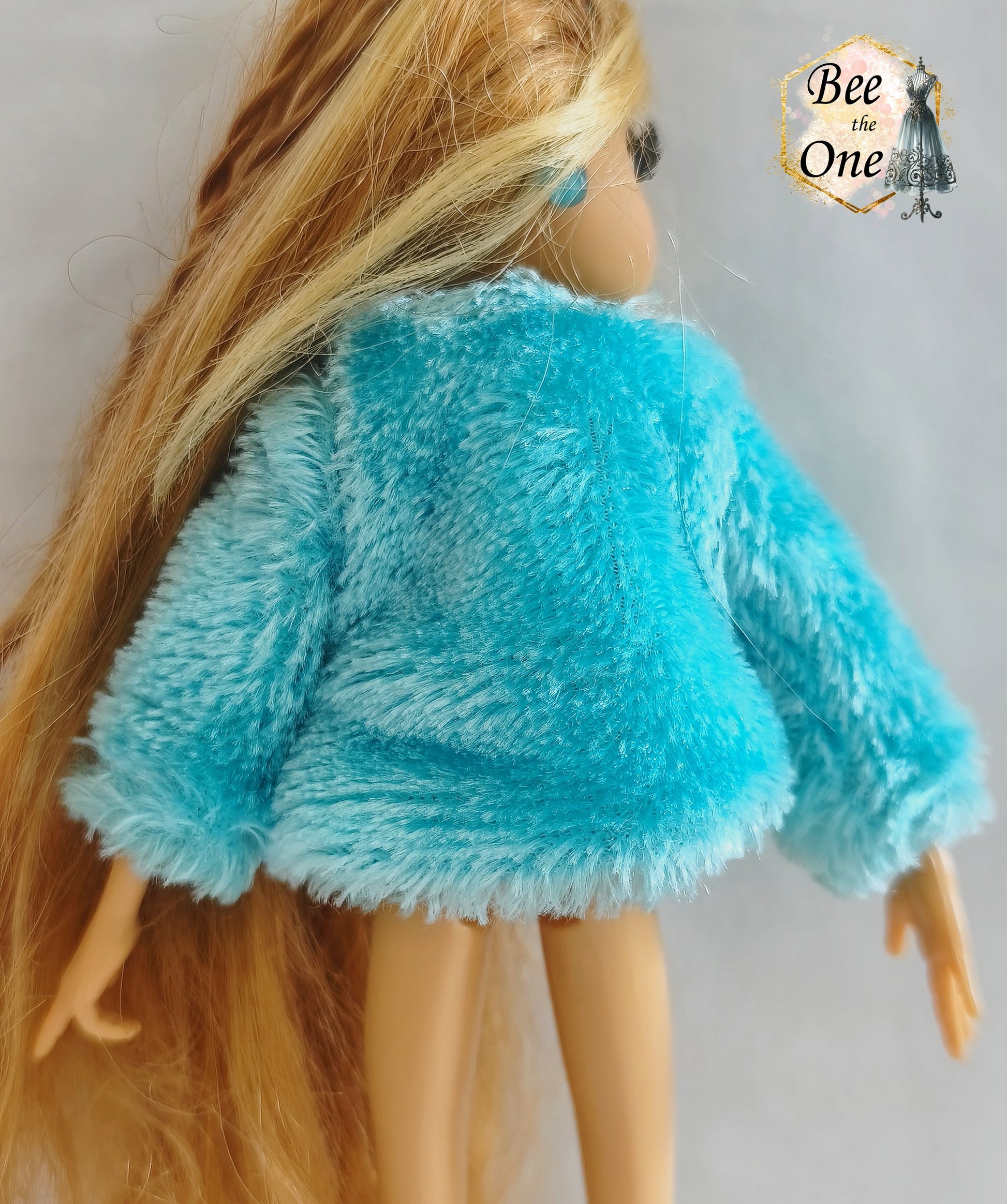 Manteau court en fausse fourrure bleu turquoise avec noeud en ruban rose satiné pour poupée Winx Club, issu du set Fairy Lounge de Mattel, porté par une poupée Flora sur fond blanc. Gros plan dos
