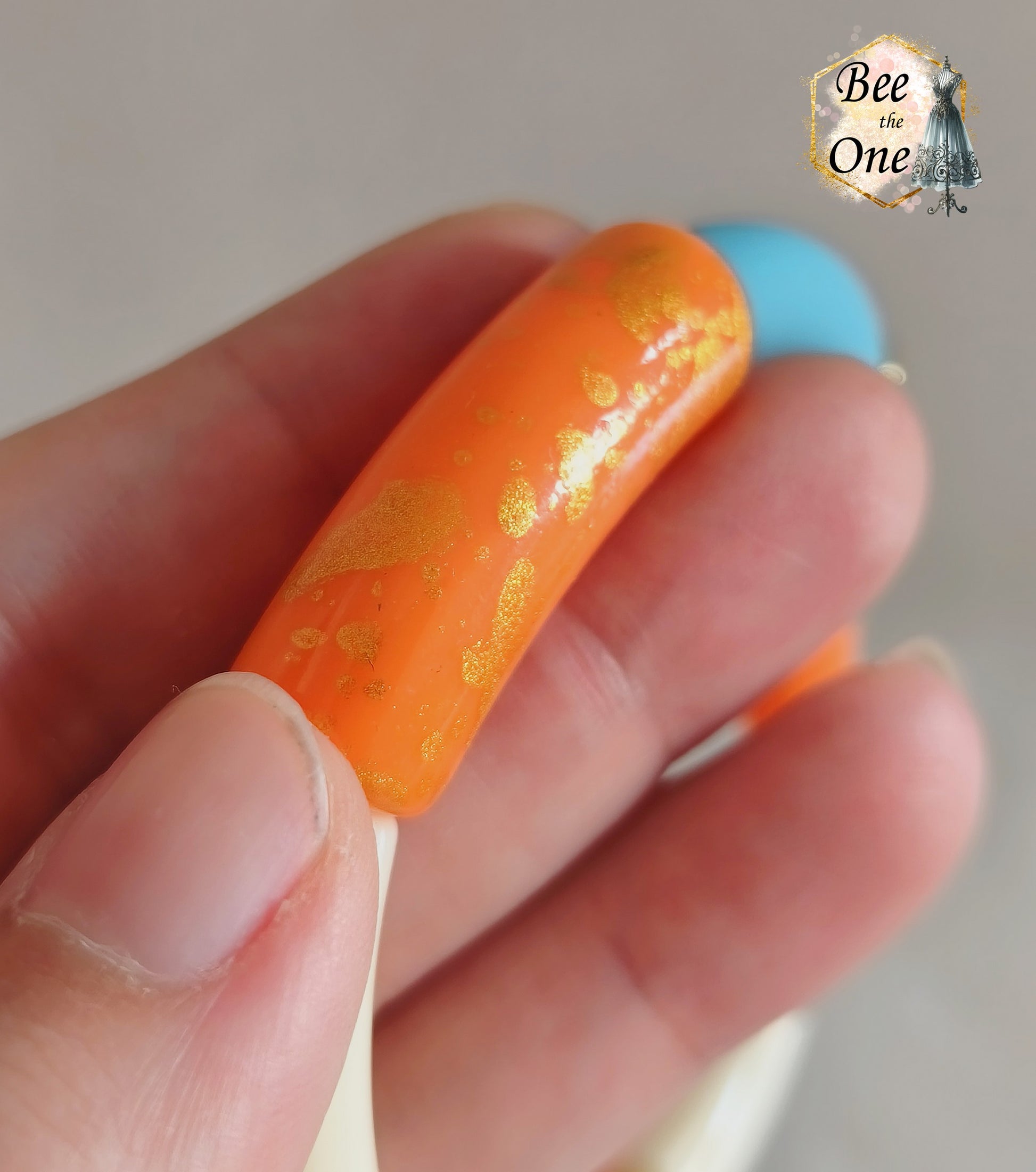 Set de trois bracelets élastiques faits main pour adulte, composés de perles tubes incurvées en acrylique aux teintes bleu azur, orange vif et crème, avec détails marbrés dorés et séparateurs dorés. Gros plan sur une perle orange à marbrures dorées en acrylique