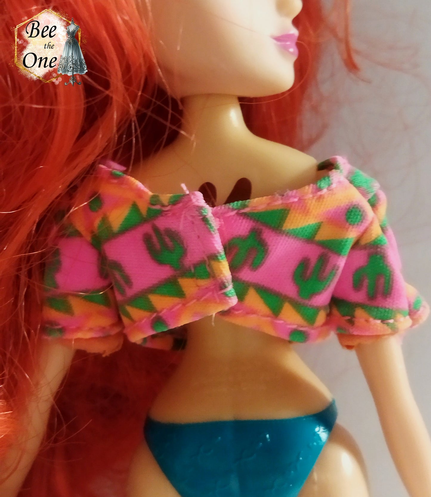 Top court pour poupée mannequin, à motif cactus et formes géométriques roses, oranges et vertes, avec liens orange et perles colorées, style bohème western. Gros plan dos