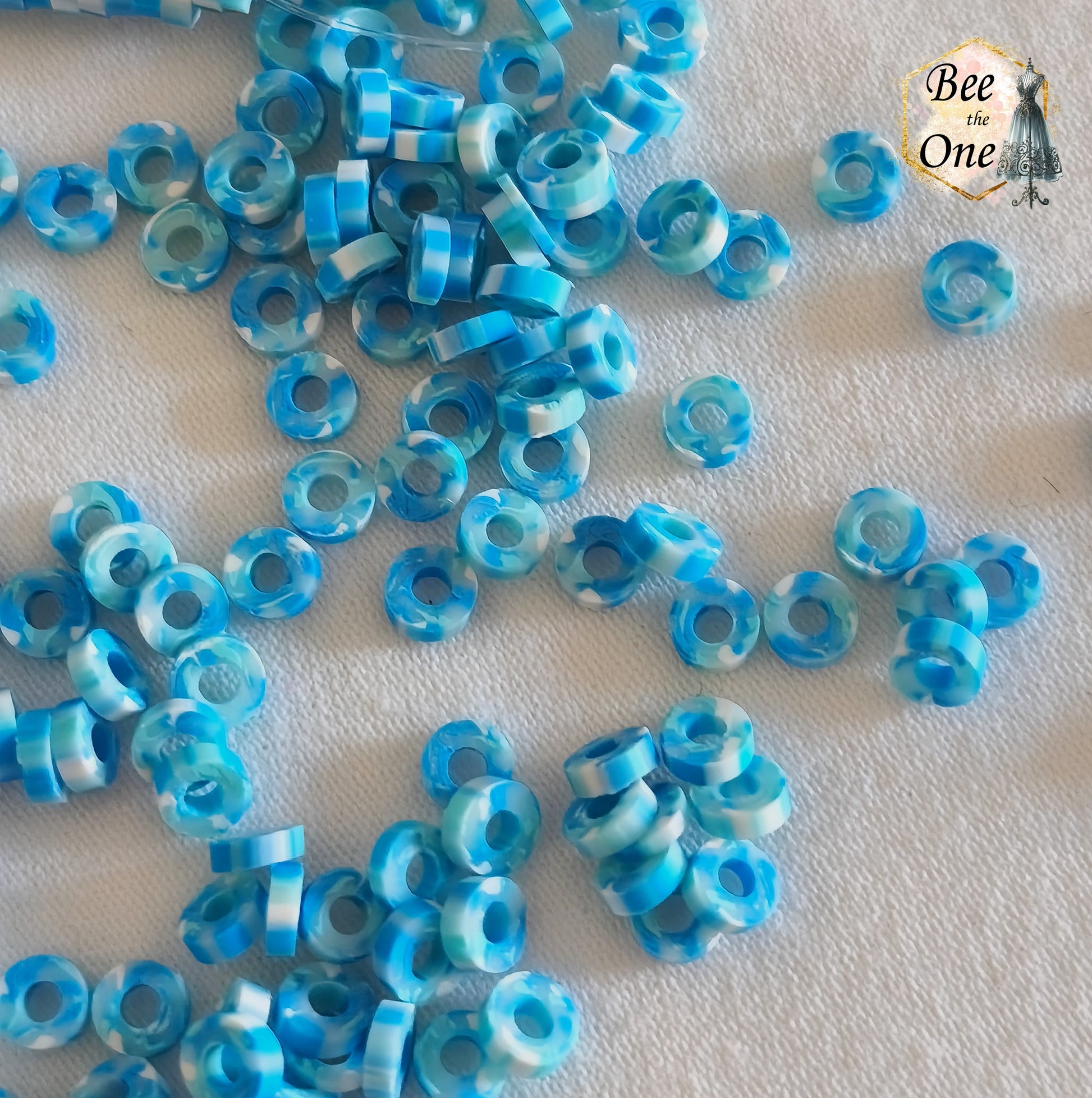 Petites perles rondelles Heishi Katsuki de 4 mm en pâte polymère, bleues, présentées sur tissu blanc. gros plan