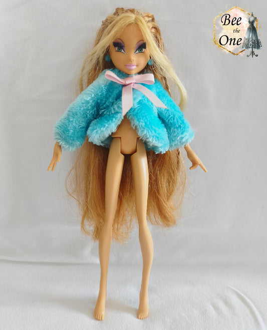 Manteau court en fausse fourrure bleu turquoise avec noeud en ruban rose satiné pour poupée Winx Club, issu du set Fairy Lounge de Mattel, porté par une poupée Flora sur fond blanc.