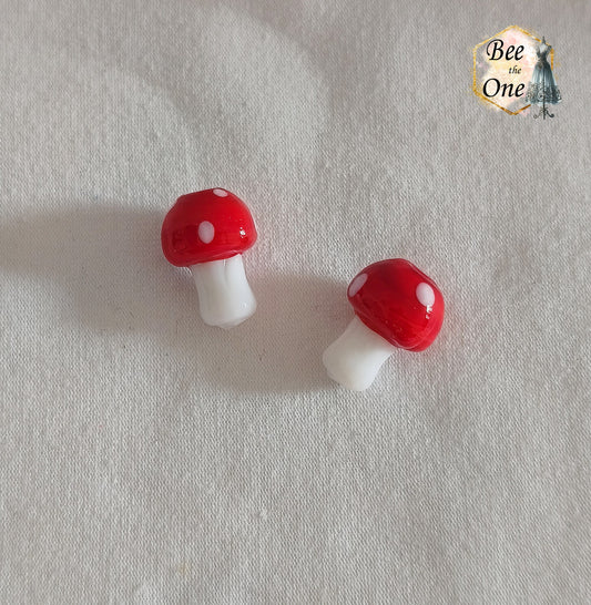 Perles en verre filé rouge et blanc en forme de champignon amanite tue-mouche à pois, percées verticalement, sur fond blanc.
