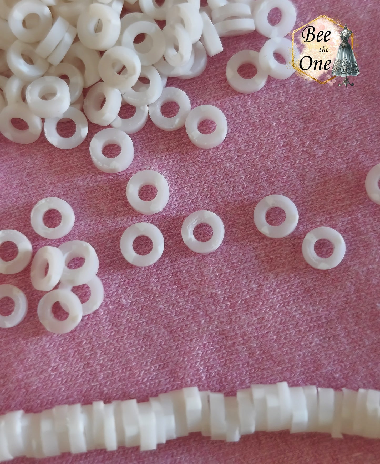Petites perles rondelles Heishi Katsuki de 4 mm en pâte polymère, blanches, présentées sur tissu rose. gros plan