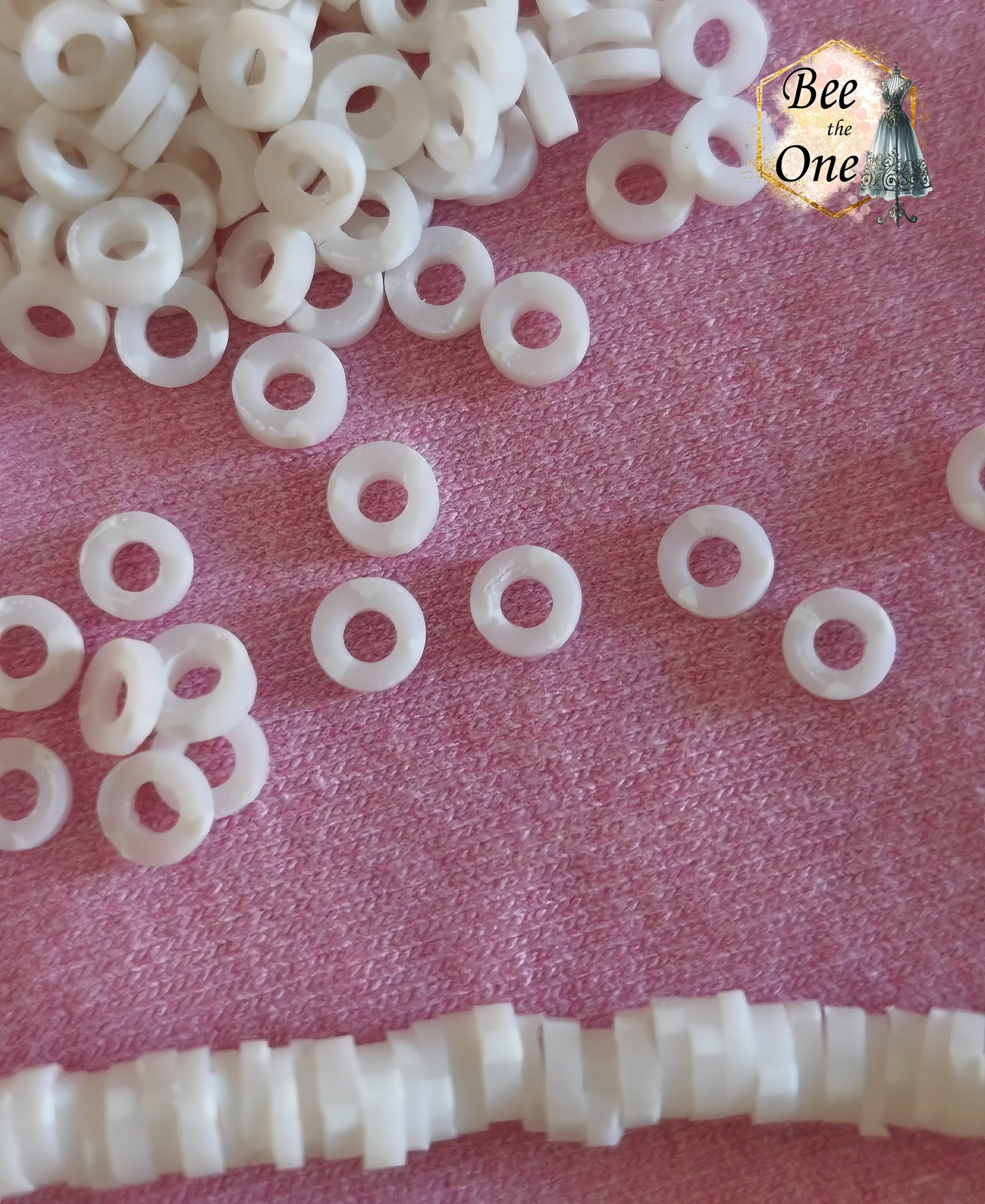 Petites perles rondelles Heishi Katsuki de 4 mm en pâte polymère, blanches, présentées sur tissu rose. gros plan