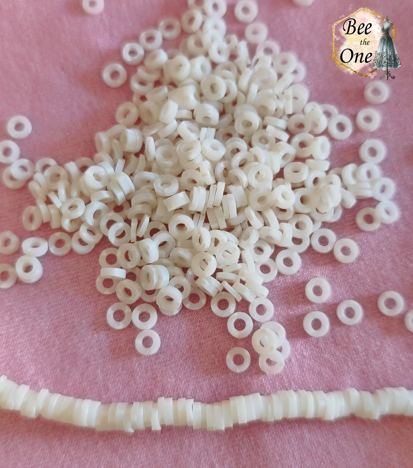 Petites perles rondelles Heishi Katsuki de 4 mm en pâte polymère, blanches, présentées sur tissu rose.